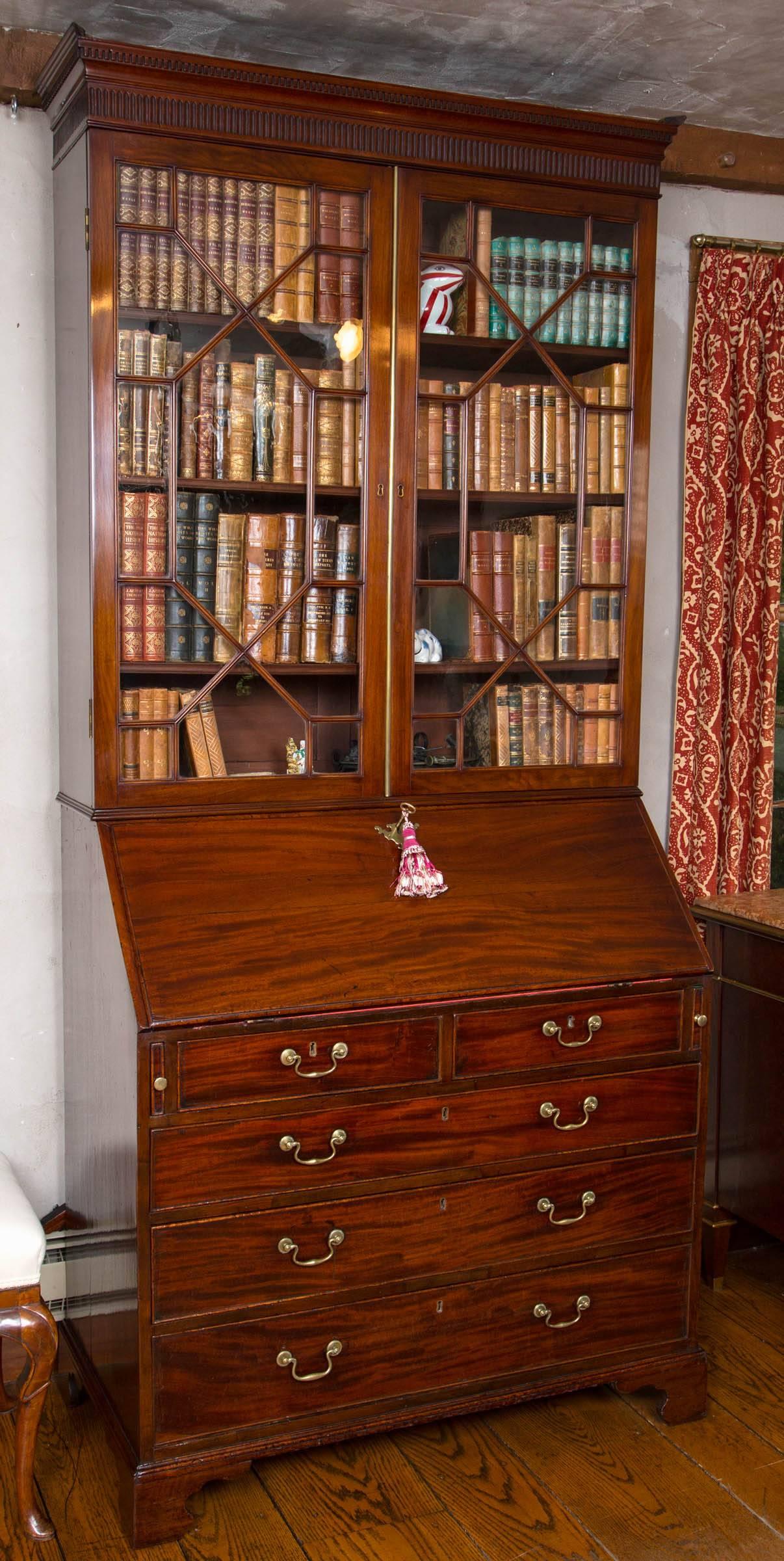 Georgian mahogany slant front glazed bookcase or secretary. The detachable broken pediment carved with dentil cornice is centered by a small platform. The upper section features two, thirteen pane, glazed doors with three original adjustable shelves