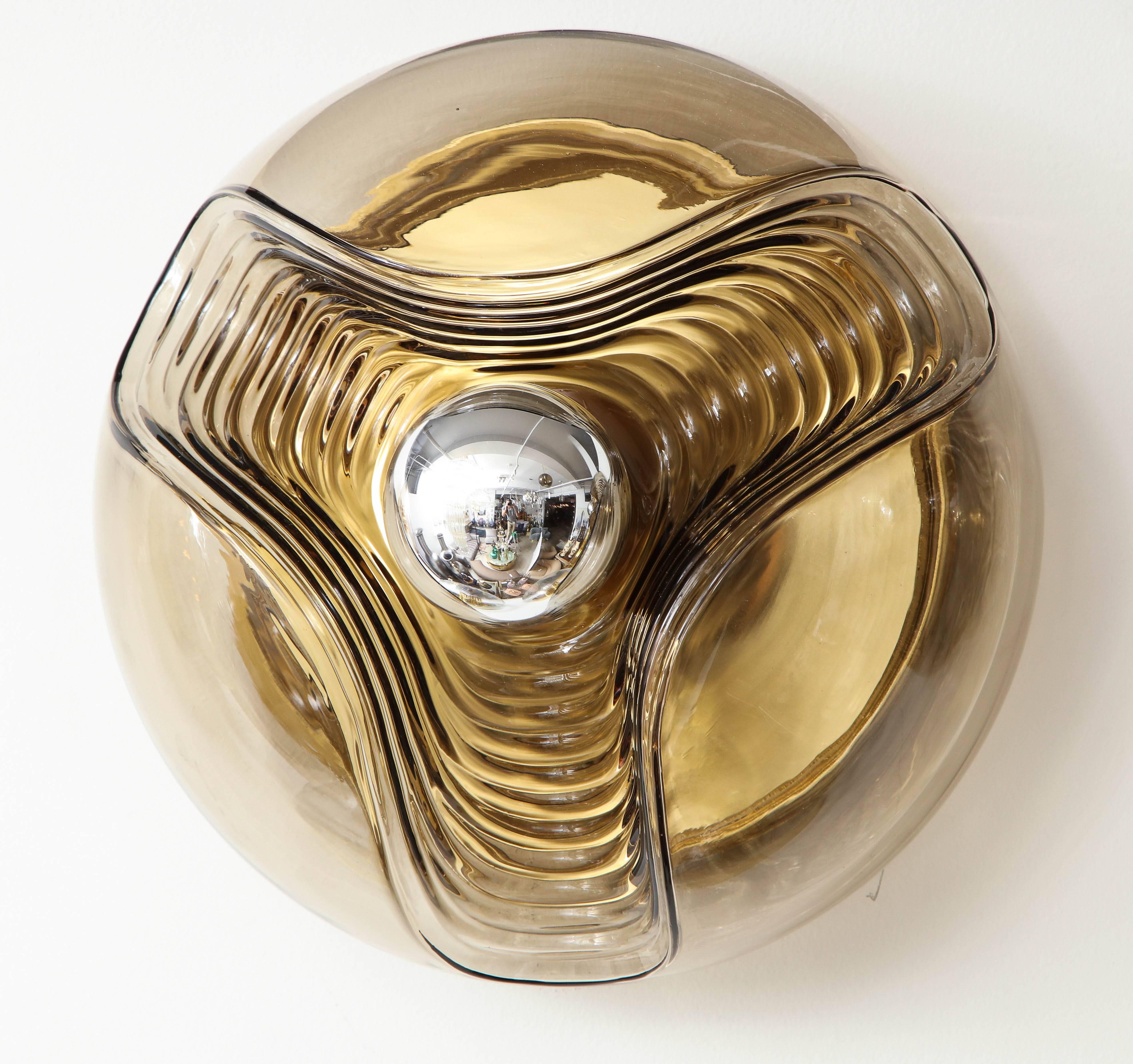 1970s, Mid-century sconce / flush mount by Koch & Lowy for Peill & Putzler.
This large smoked wave form glass shade is supported by a brass plate with a single centre light bulb.
The fixture has been newly rewired for the US and takes a