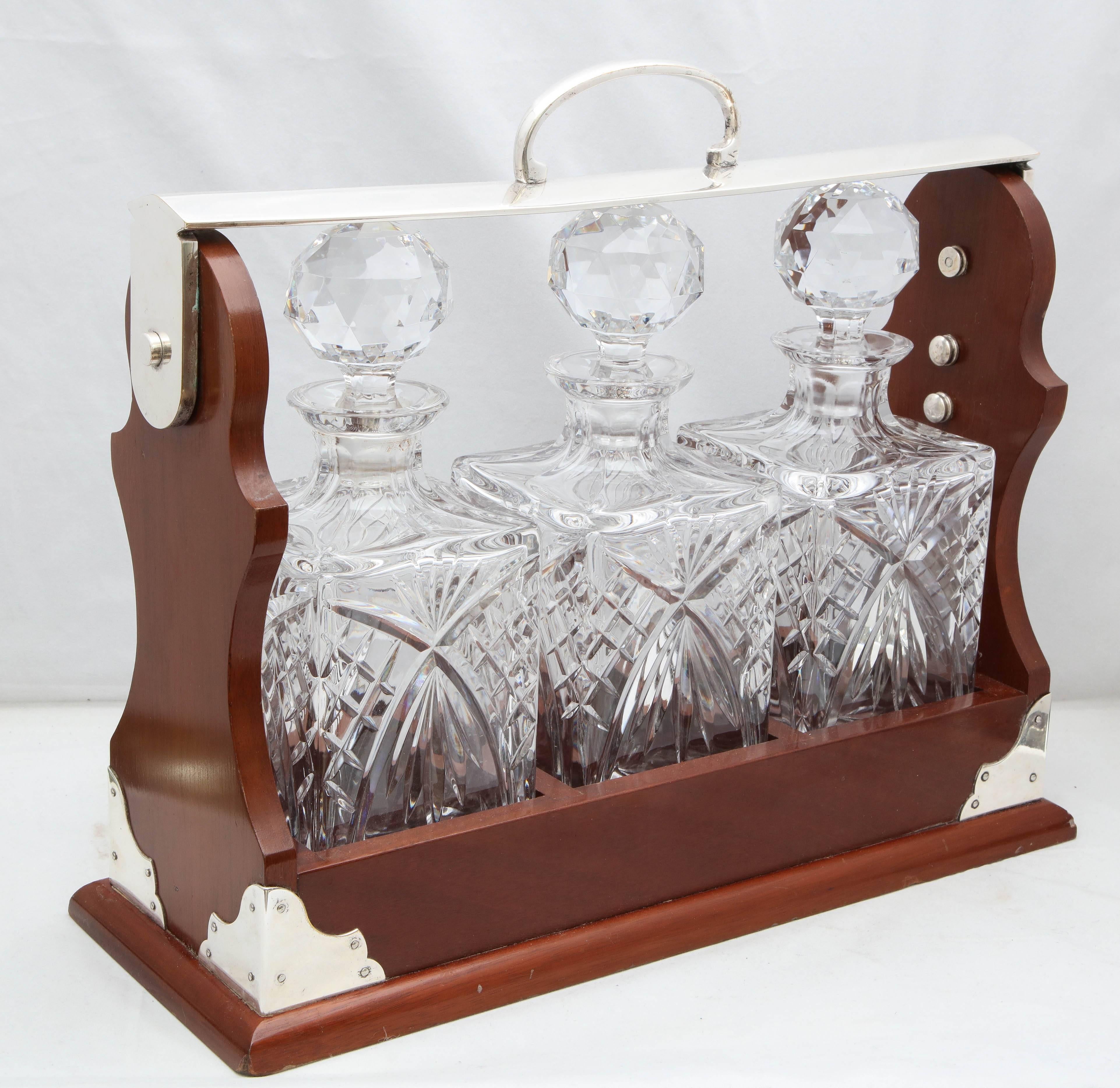 Edwardian, silver plate mounted wood, three decanter Tantalus, England, circa 1905. Case measures 15 inches wide x 6 inches deep x 13 1/4 inches high to top of handle. Each glass decanter measures 10 1/2 inches to top of stopper x 3 3/4 inches wide