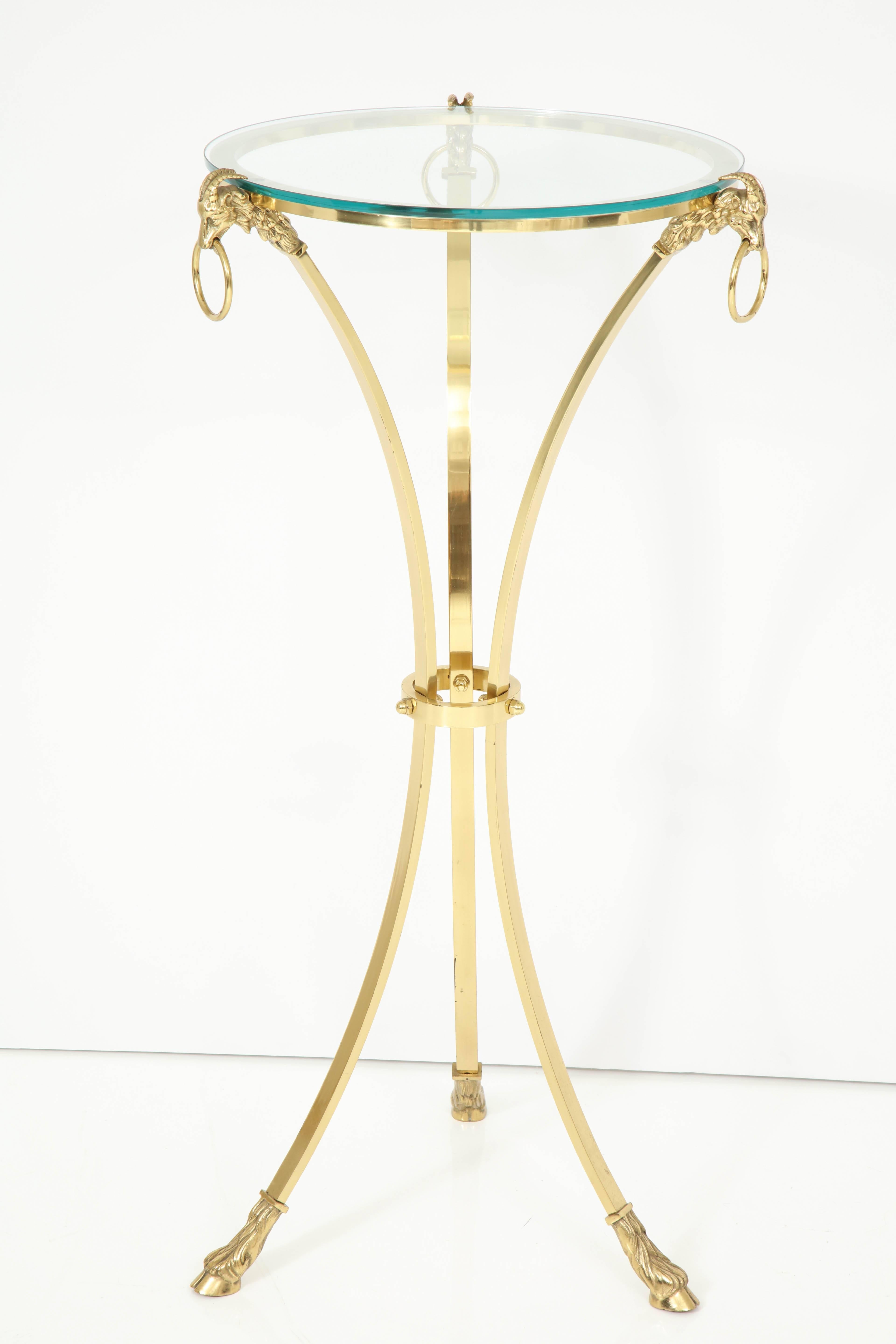 A midcentury side table attributed to Maison Charles, with glass top is supported by three brass legs detailed with rope banding and hooved feet.
