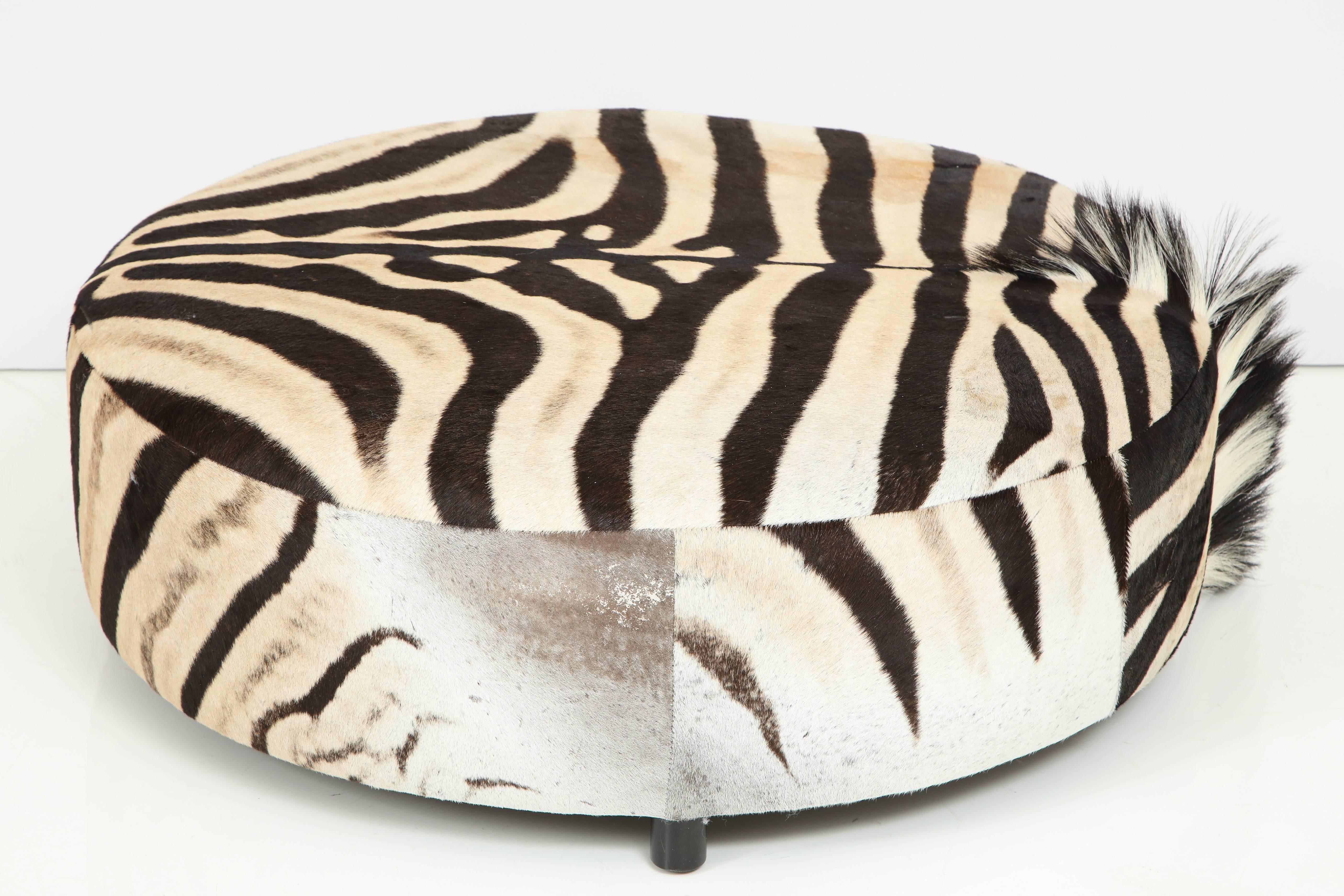 Decorative round zebra hide ottoman. Beautifully showing of the man on one side.
Dark chocolate colored round wood legs.
