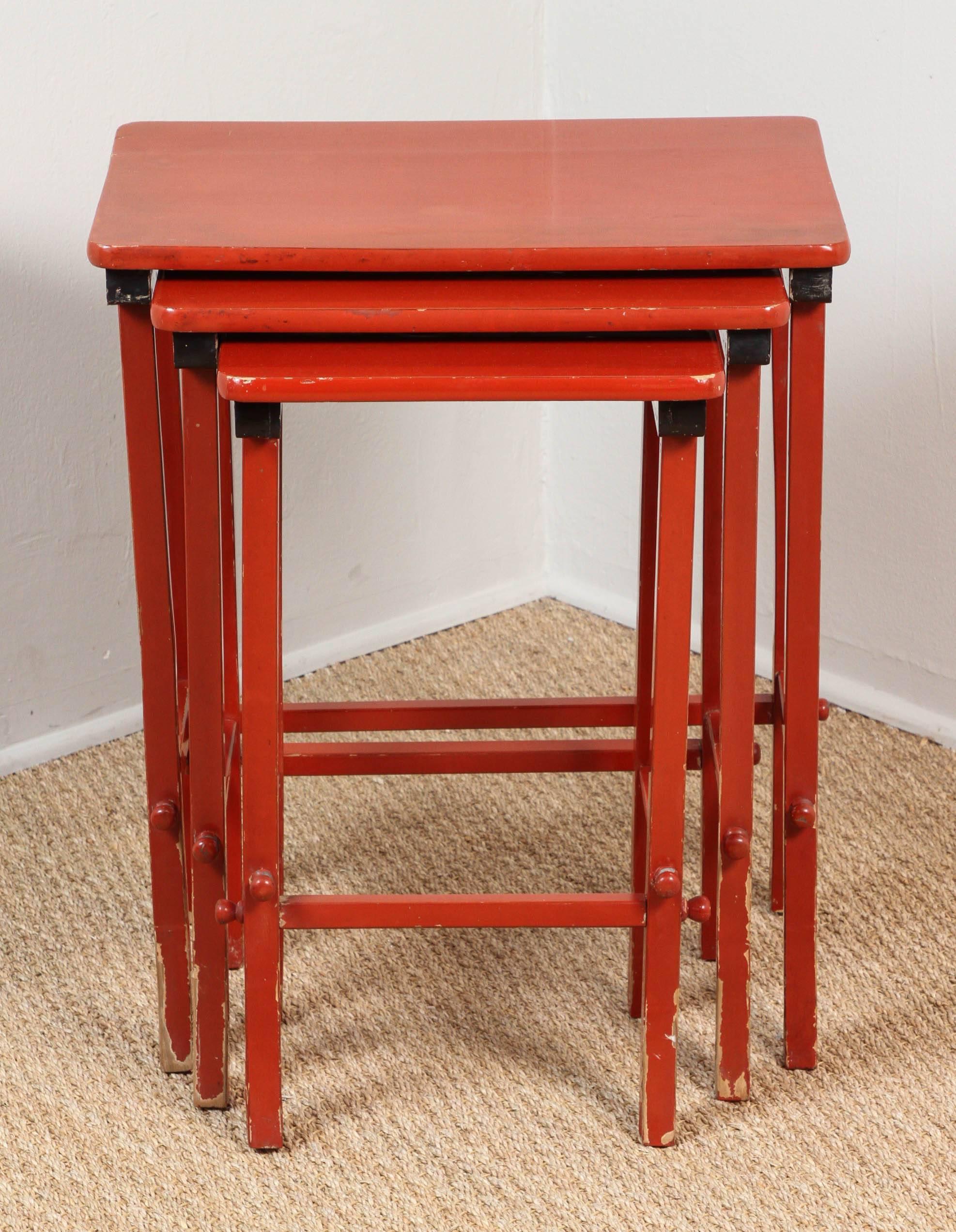 Set of three slightly distressed red and black lacquer nesting tables.