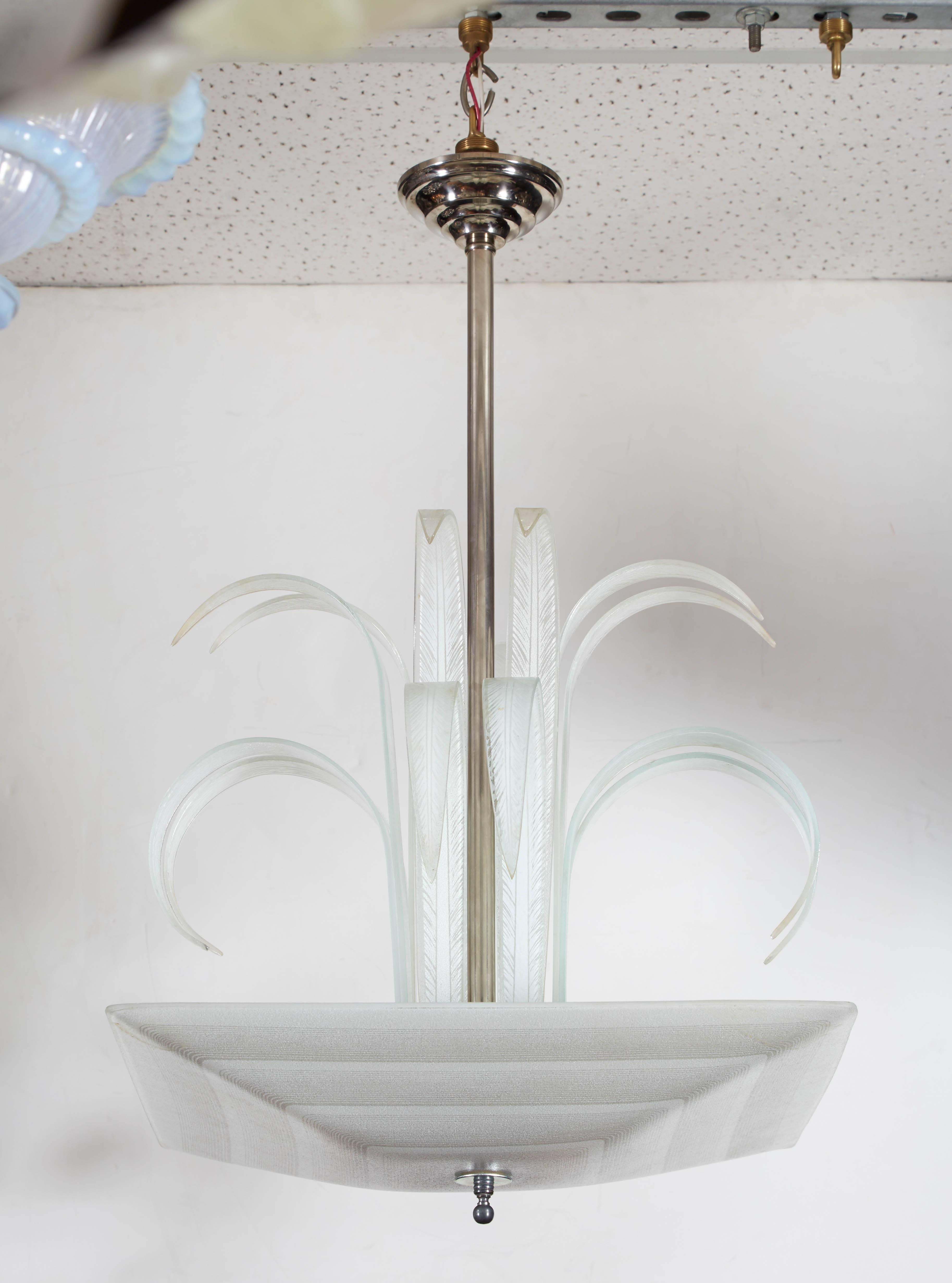An unusual chandelier of organic modern design with dramatic crown plume of curled glass leaves in feathery palmette formation, surrounding a nickeled center stem, while holding a matching etched, stepped grey and white square bottom glass.
Can be