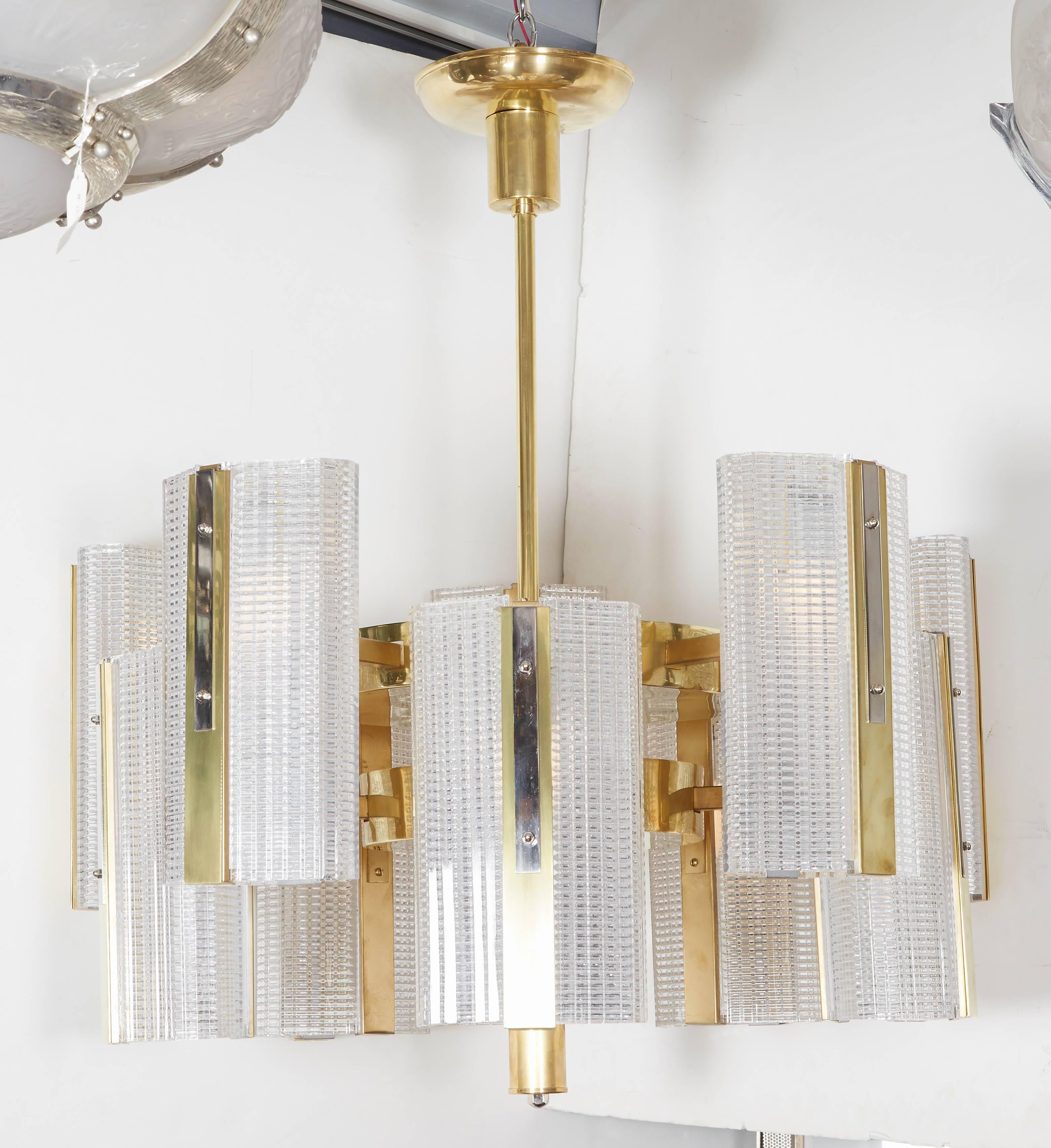 Pair or single available
Very large modernist highly architectural ten arm chandelier comprising bi level rectangular boxes of interlacing lines in a grid pattern mounted in a polished brass armature.
The crystal glass boxes glisten and shimmer in