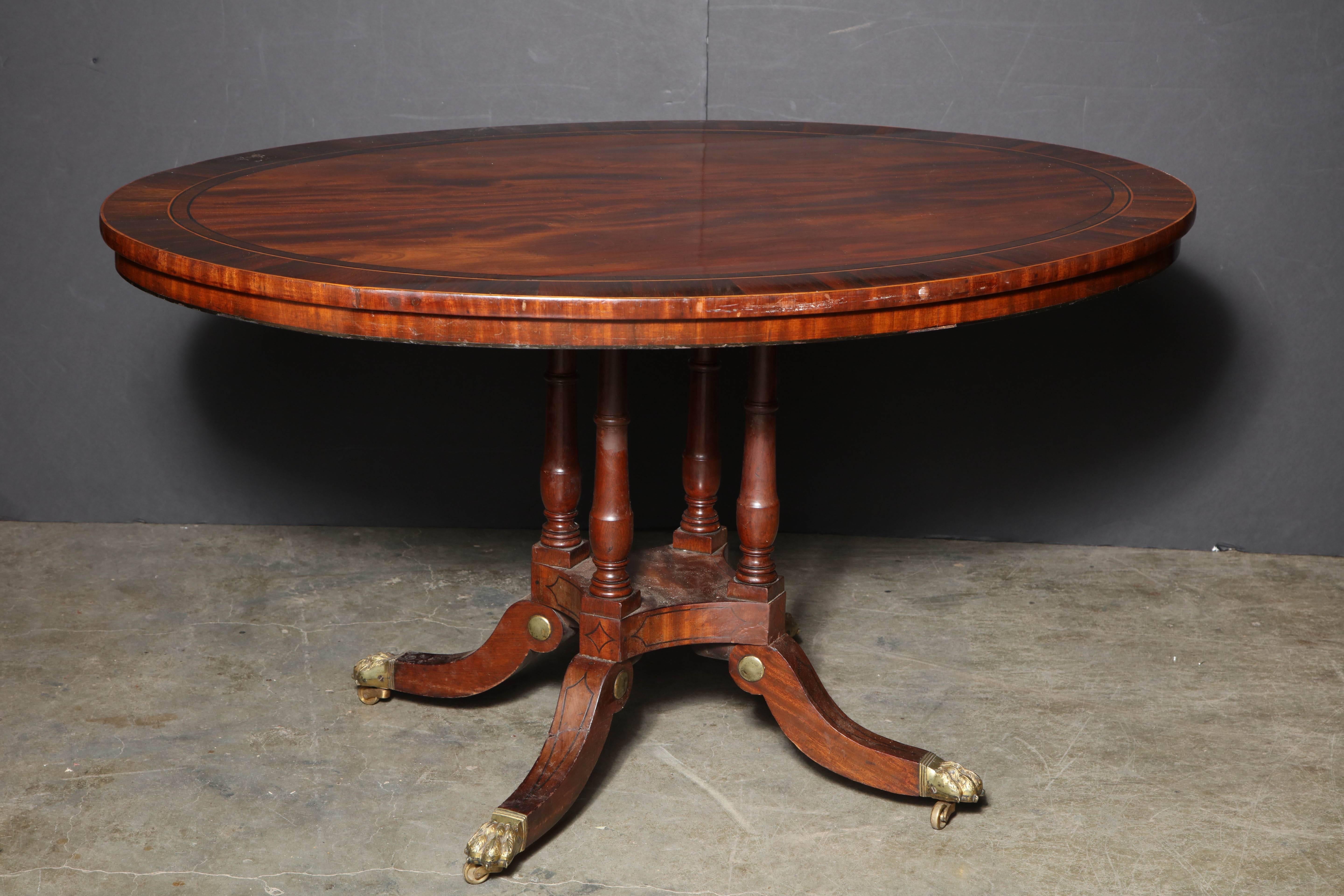 Regency mahogany rosewood crossbanded tilting oval centre table with a four-column pedestal base, intricate buhl brass inlay on brass paw foot casters.