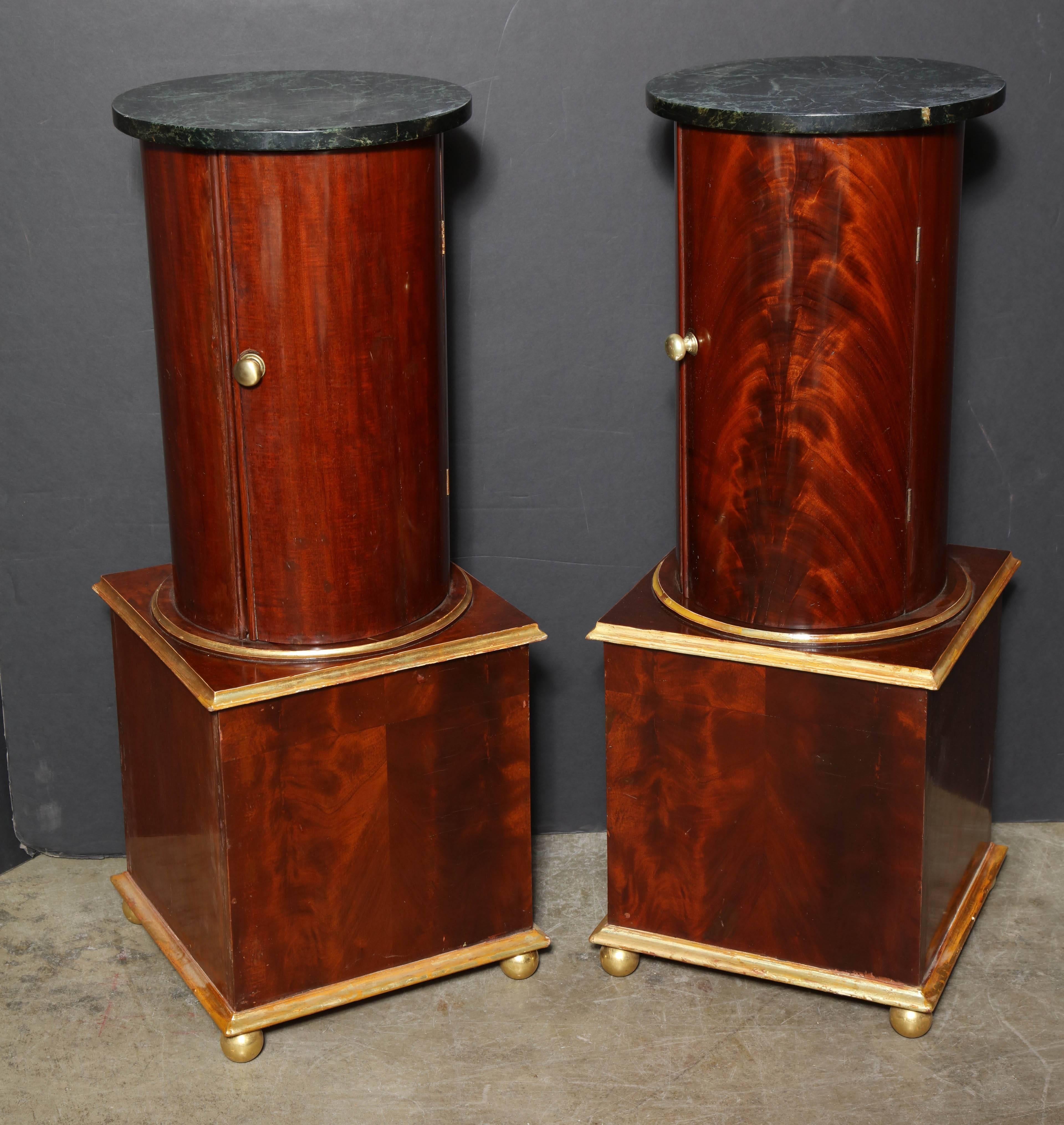 Pair of Baltic marble-top mahogany cylinder form cabinet pedestals on square gilded bun foot bases.