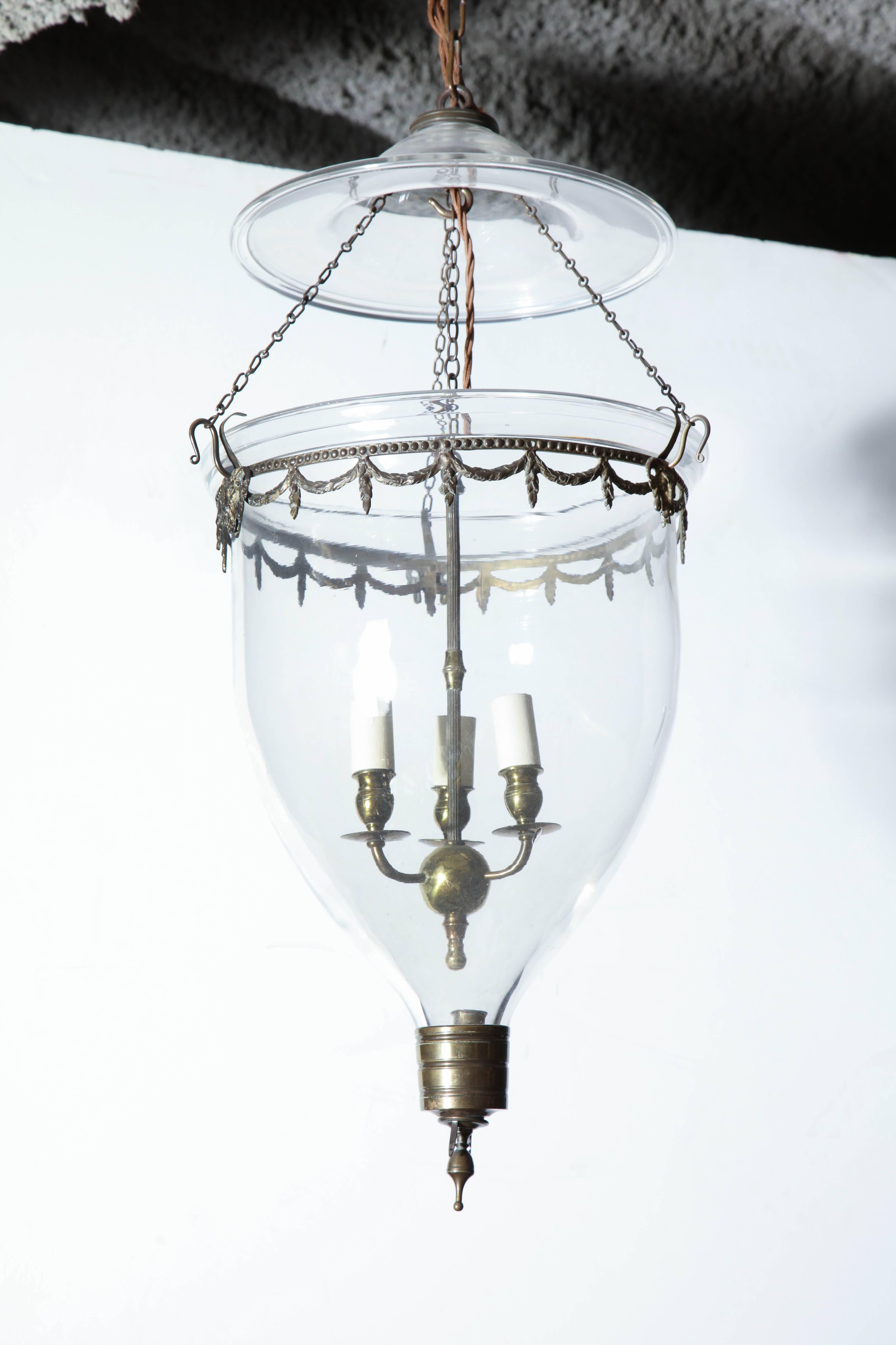 Classic shaped bell jar lantern with bronze drapery banding, brass segmented base, three-light cluster and ram's head S form hooks.