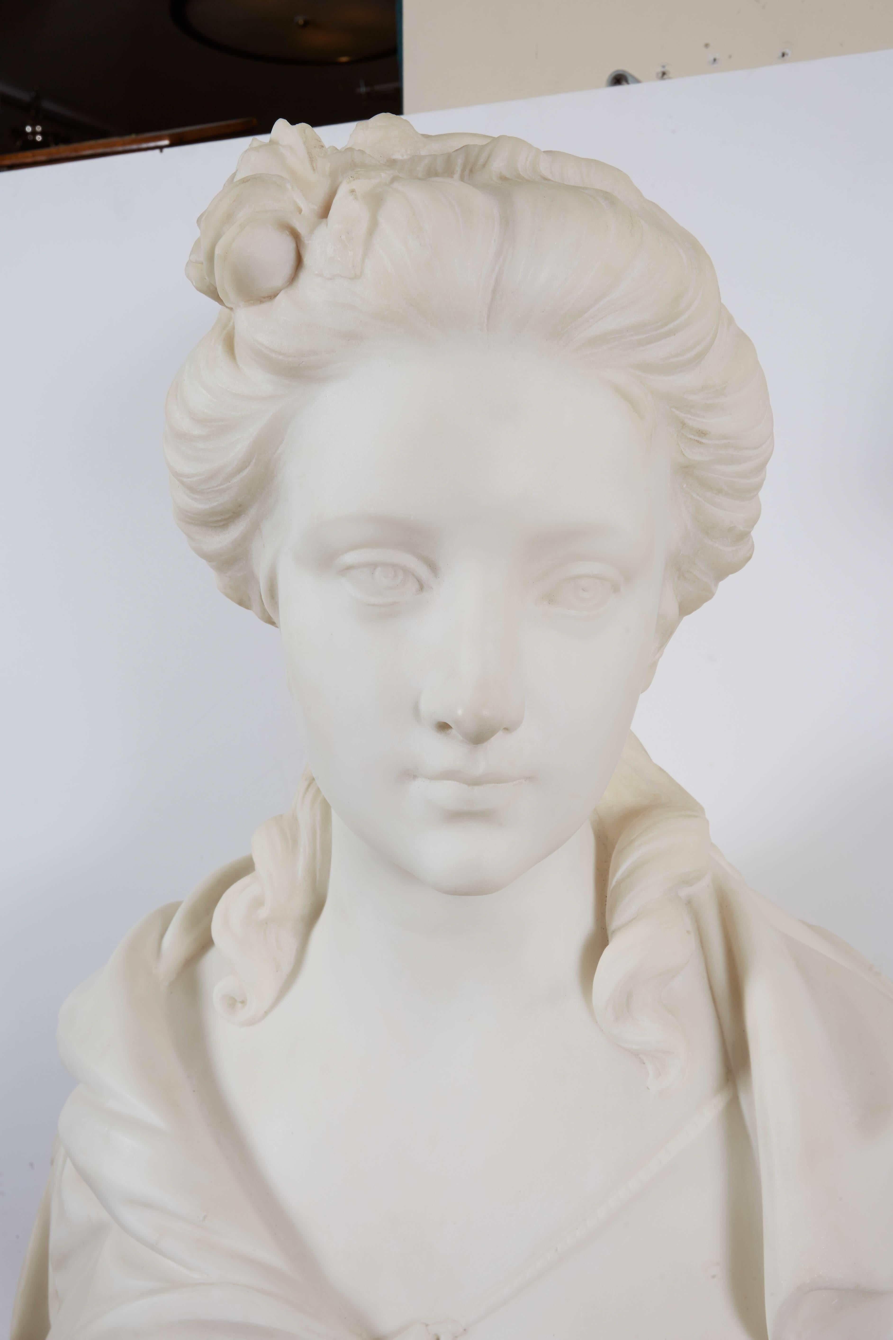 A carved marble bust of a woman, on waisted marble socle, flowing hair and loose drapery.
 