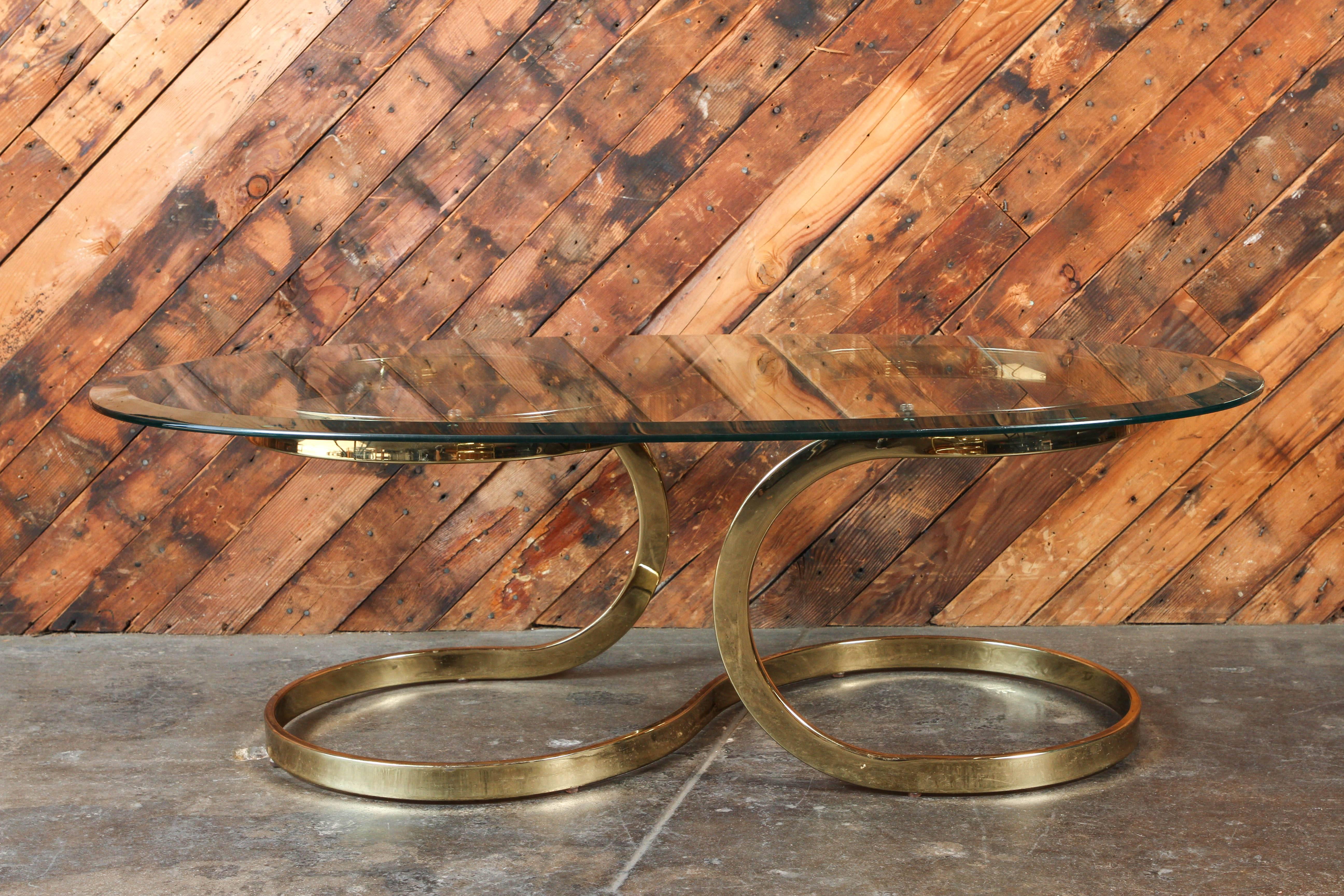 Hollywood Regency vintage brass ribbon coffee table with glass top
In the manner of Milo Baughman. Maker unknown, but still fabulous and a great design. Includes oval glass top with beveled edge,
1970s-1980s.  

