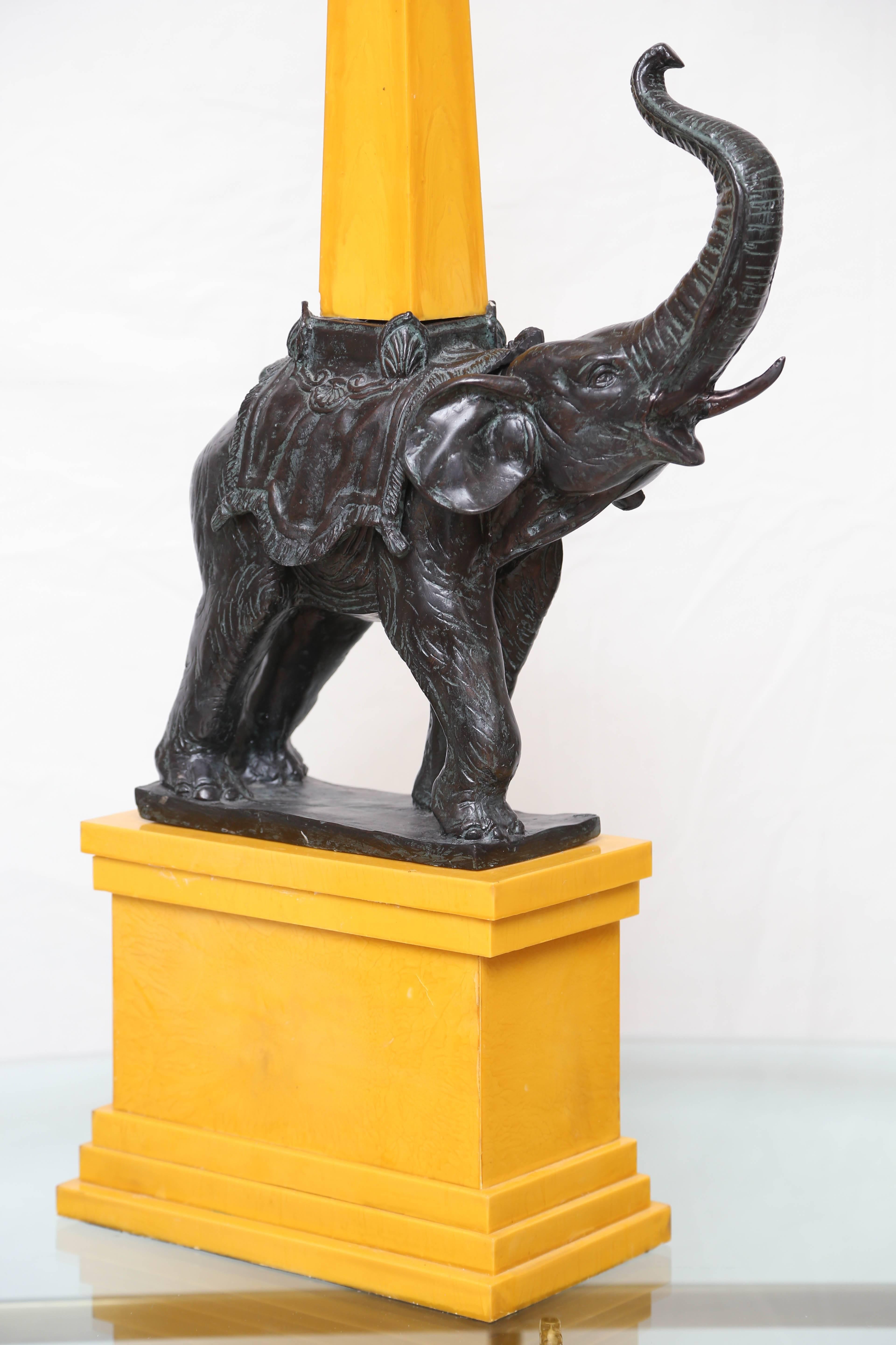 Imposing elephant standing on yellow faux marble base with obelisk on top.