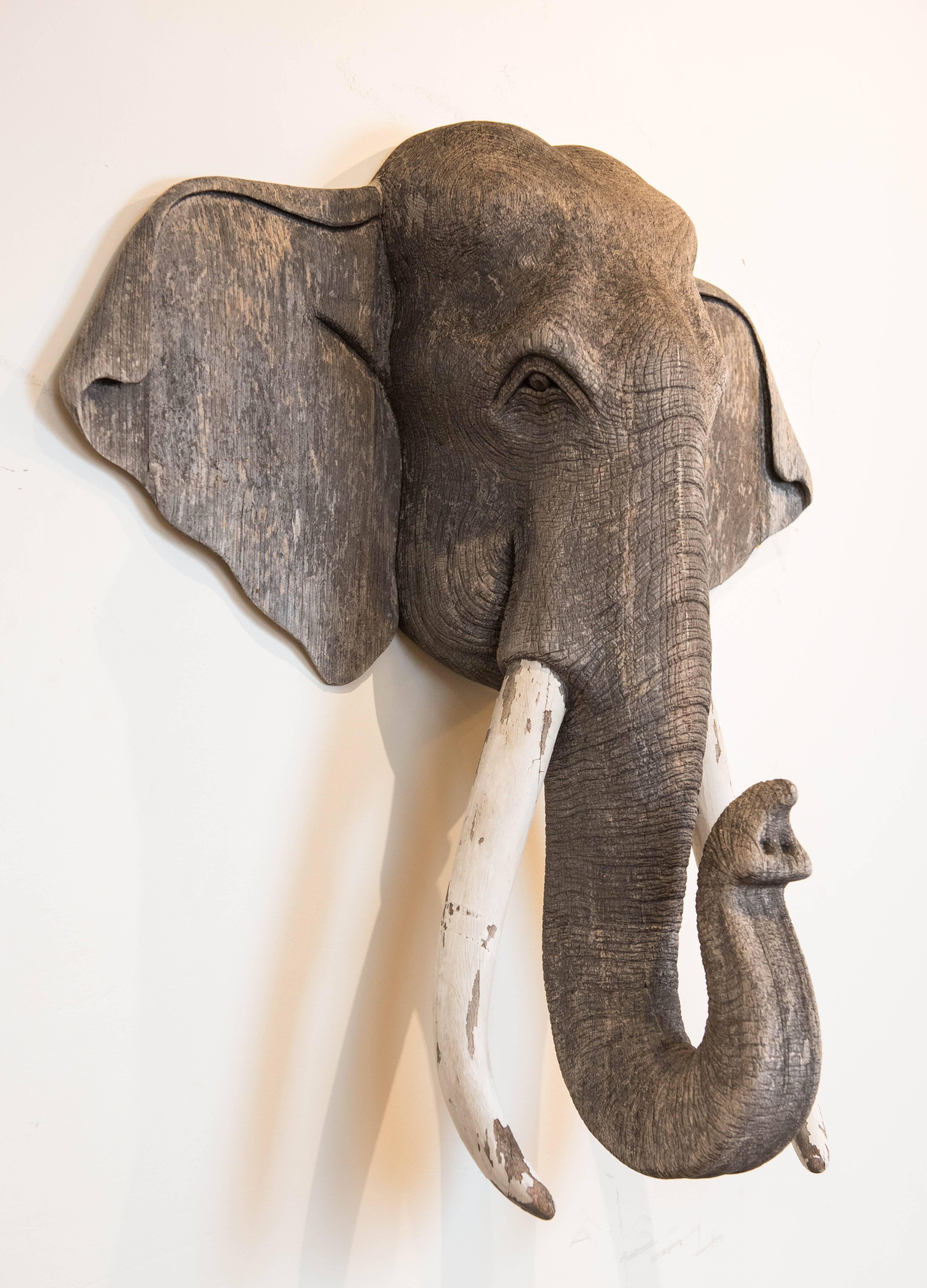 This magnificent wood wall-mounted elephant carving has an authentic weathered patina that only years of outdoor exposure can create. It has a gorgeous grey color and its wood tusks show wear consistent with it's age and exposure. It was brought