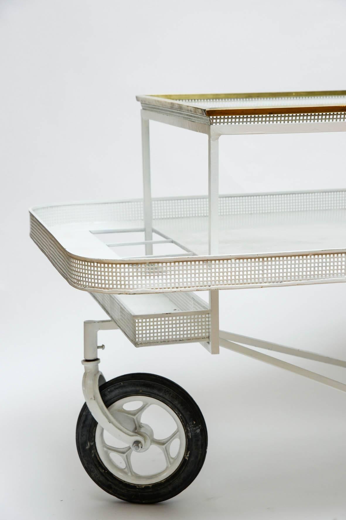 Original three wheels trolley with two levels including a removable tray with brass setting. Three dedicated spots for bottles.

In the style of Mathieu Mategot in white perforated enameled metal.
