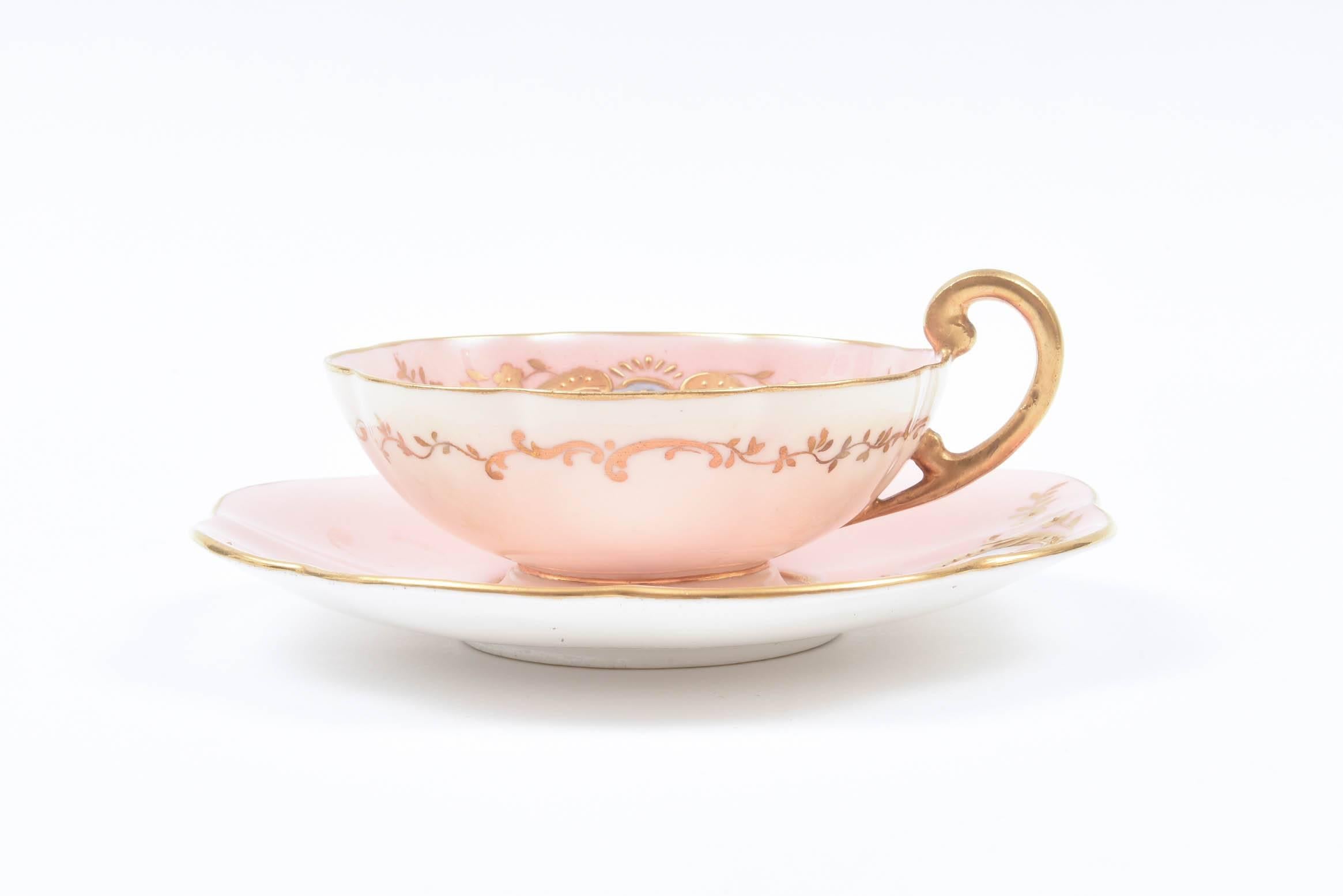 A charming antique circa 1900 blush pink cup and saucer with cartouches of hand painting encircled with raised tooled gilding. A scallop shape, ear form handle and pedestal foot adding to its appeal. In very nice antique condition and perfect for