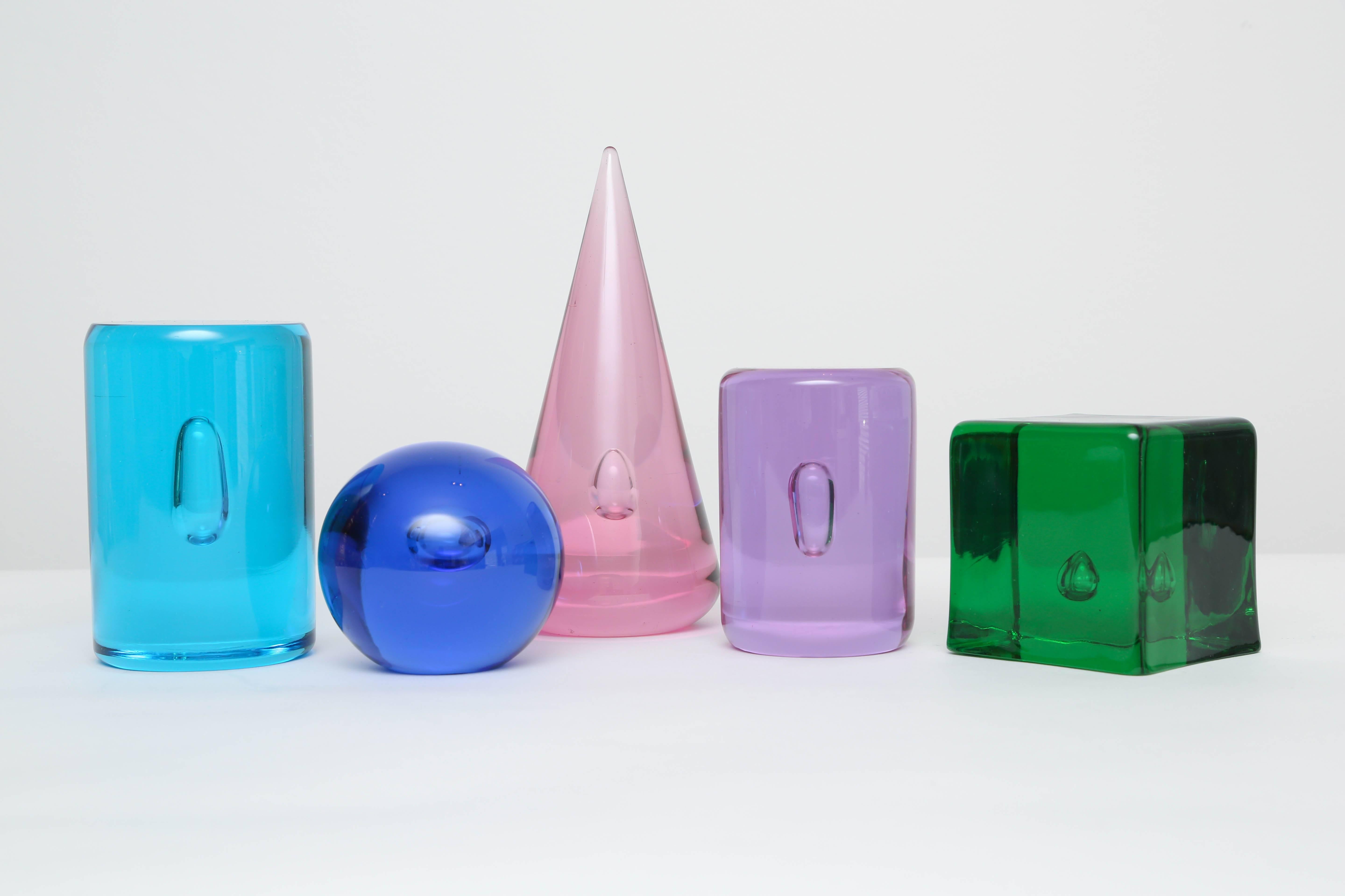 A colorful tabletop sculpture group consisting of a cube, cone, sphere and two cylinders each encasing a perfect air bubble. The jewel-tone colors are amethyst, sapphire blue, rose, emerald and aquamarine. 

The tallest of the figures is 9