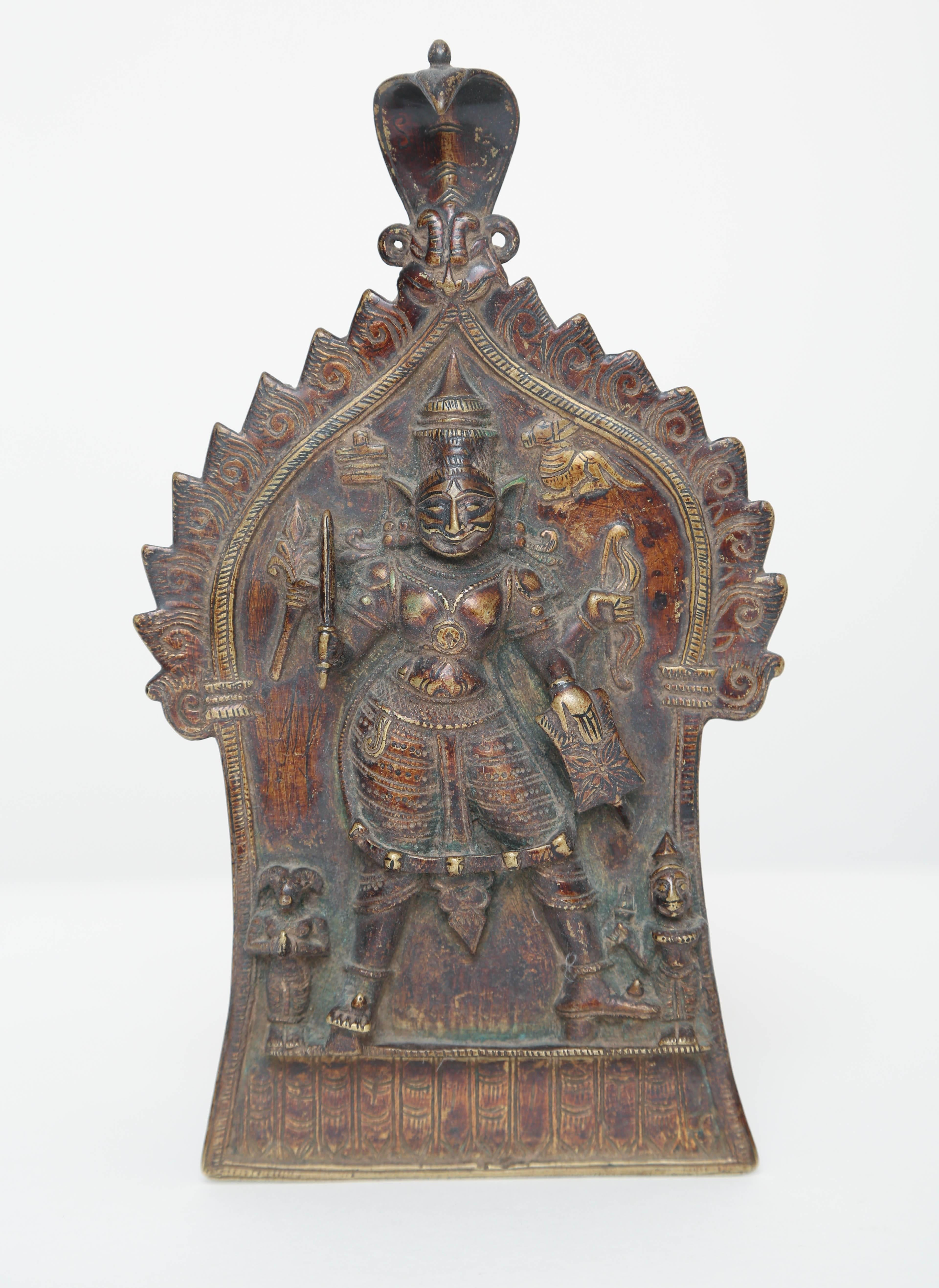 Durga is the warrior goddess in the Hindu culture, she is the protector of the good depicted here mulit-armed with a sword, shield, bow and arrow, astride two male attendants all set within a temple with the sacred cobra presiding above.