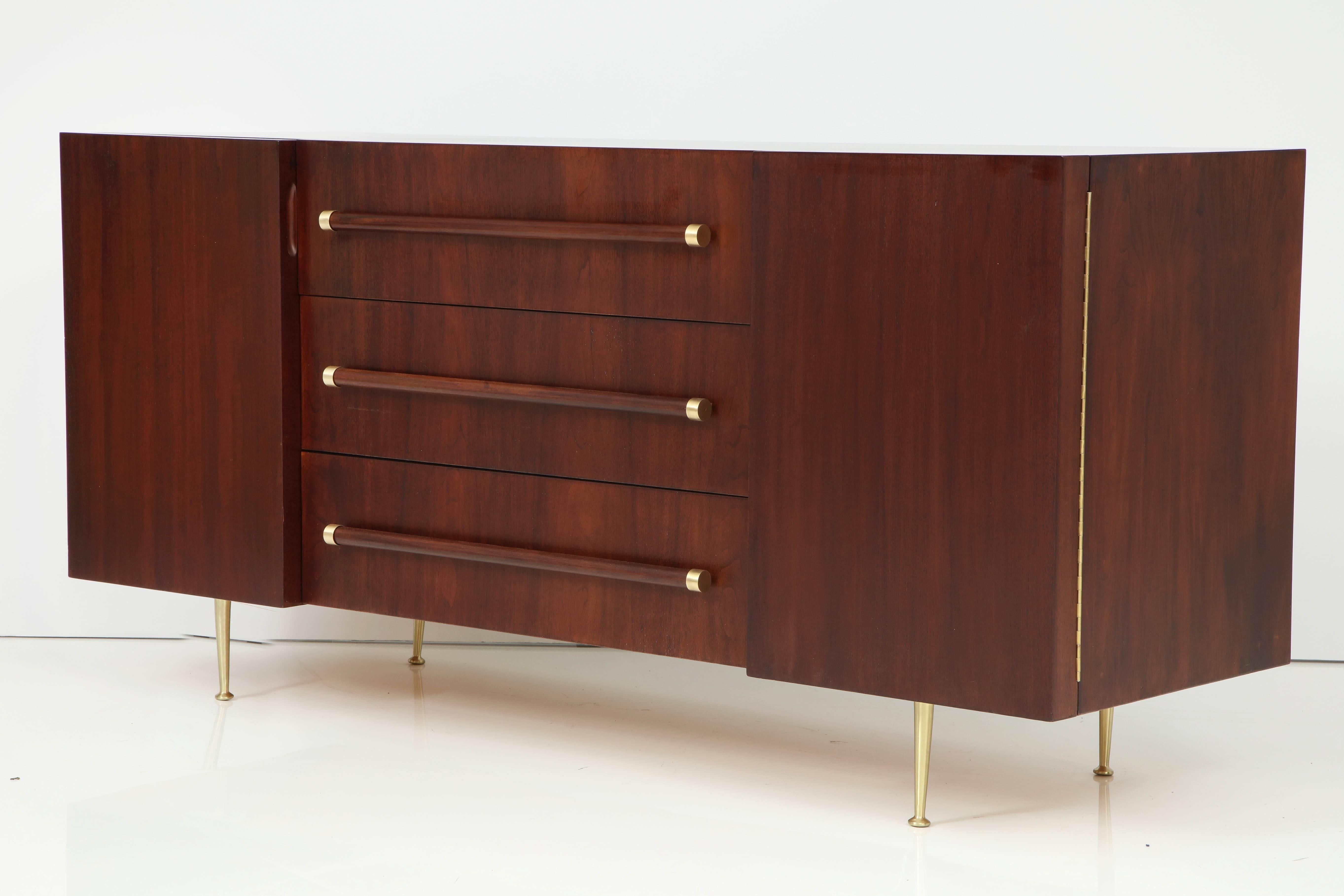 Midcentury classic sideboard/server with a medium brown stained walnut case, three drawers with walnut dowel pulls with brass end caps and two side compartments each concealing an adjustable shelf, satin brass legs finish off the piece. Mint