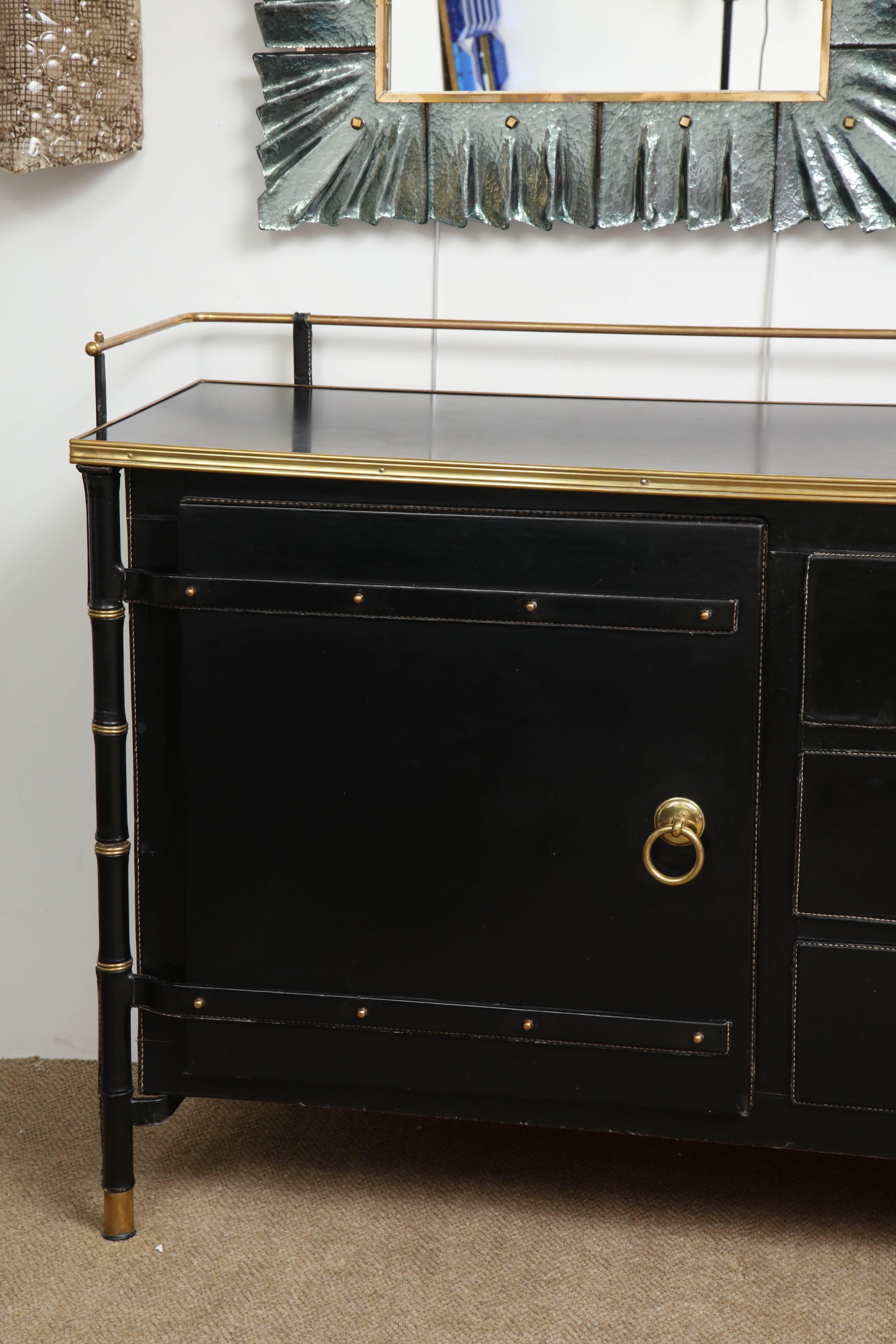 Rare and fine black hand-stitched leather by Jacques Adnet. Two doors on each side concealing shelves, suite of three drawers in the center. Solid brass handles. Oak interior.
France 1950's