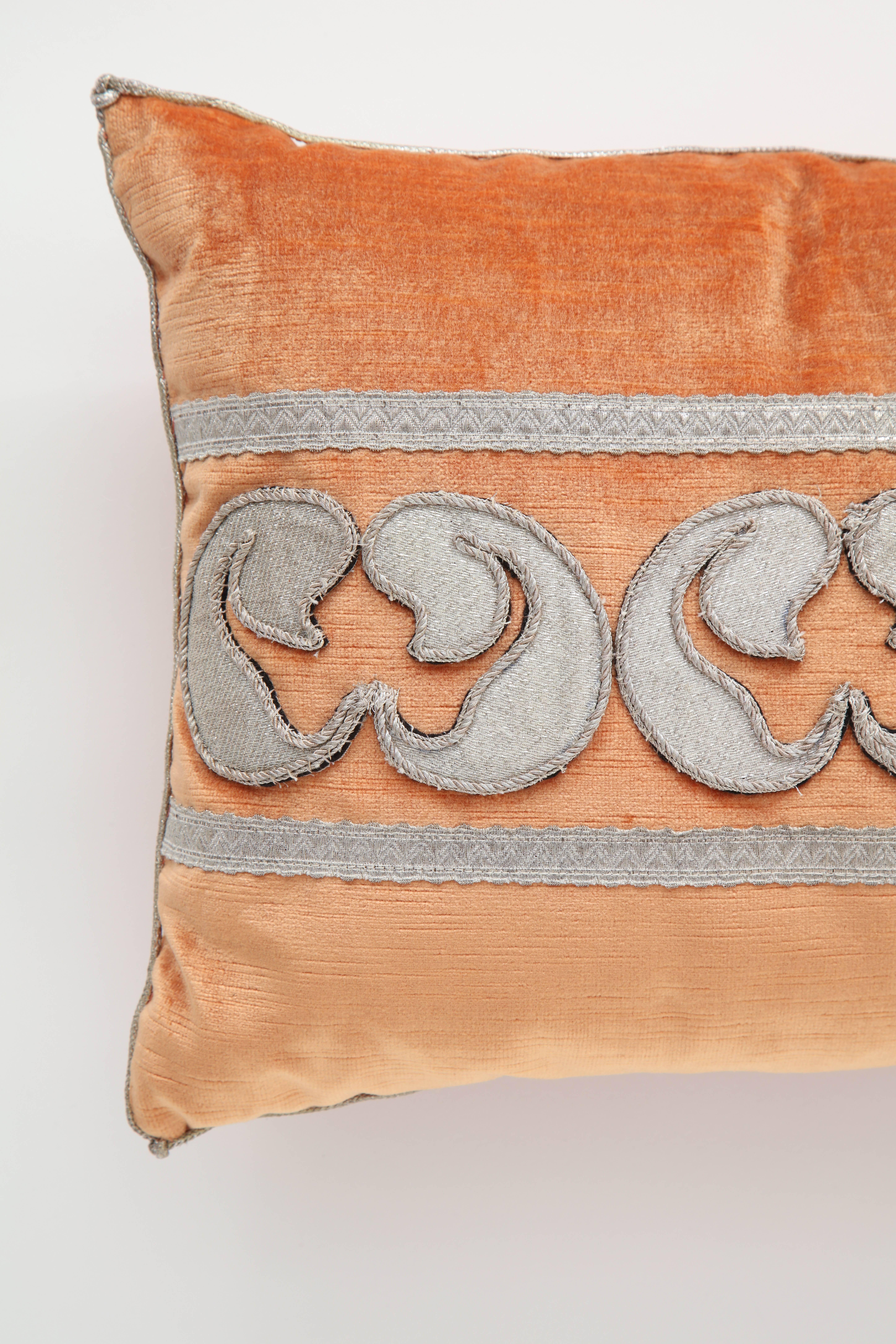 A stunning pillow in a tangerine velvet accented with antique metallic fragments forming a design between a border of antique metallic trim. Hand bordered in a metallic cording and down filled. Created by BViz Design.
