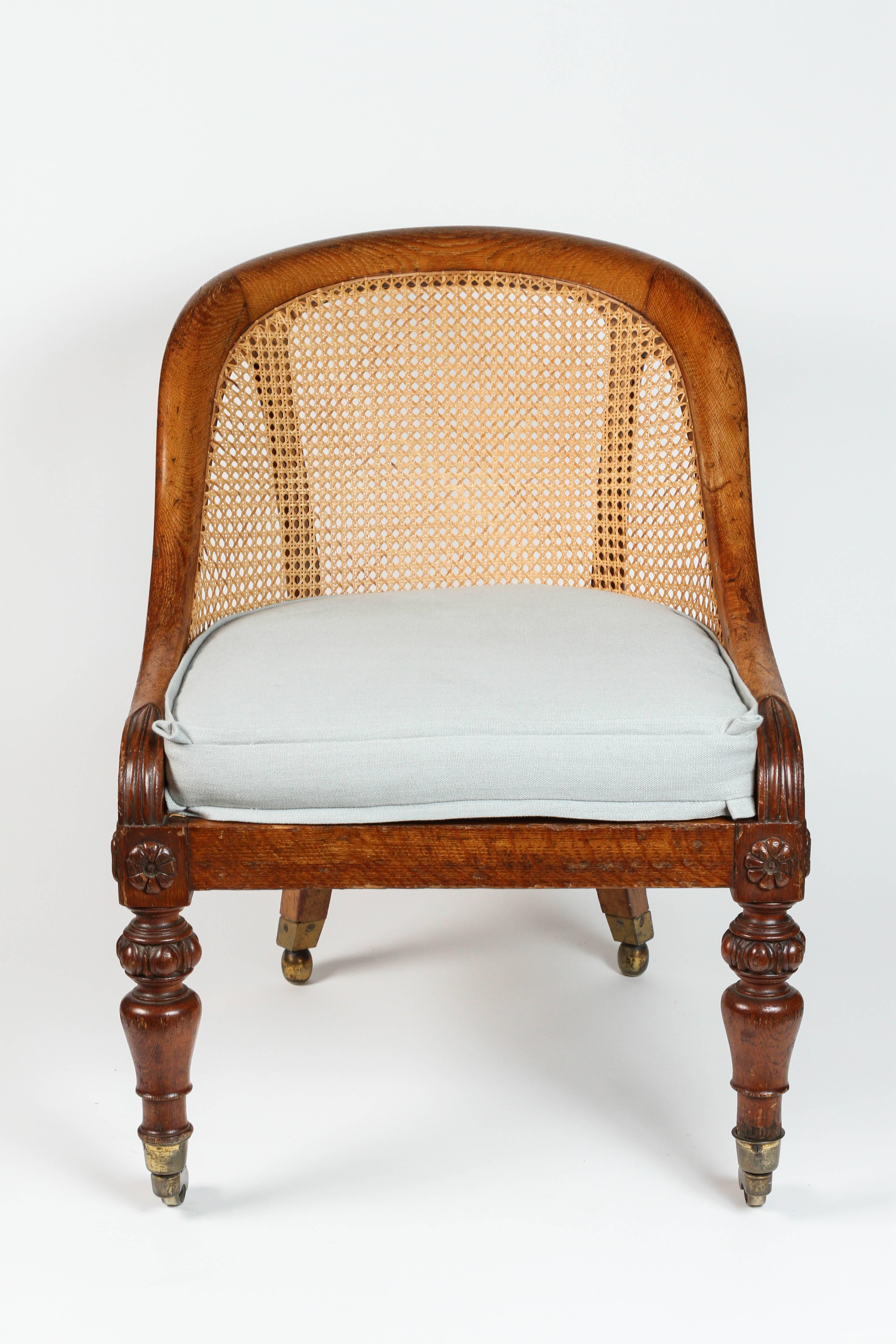 A handsome pair of English caned spoon-back chairs that date from the 1830s. They have elaborately carved front legs, and curved back legs that are on casters. The seat cushion is newly upholstered in a nest egg blue linen fabric.