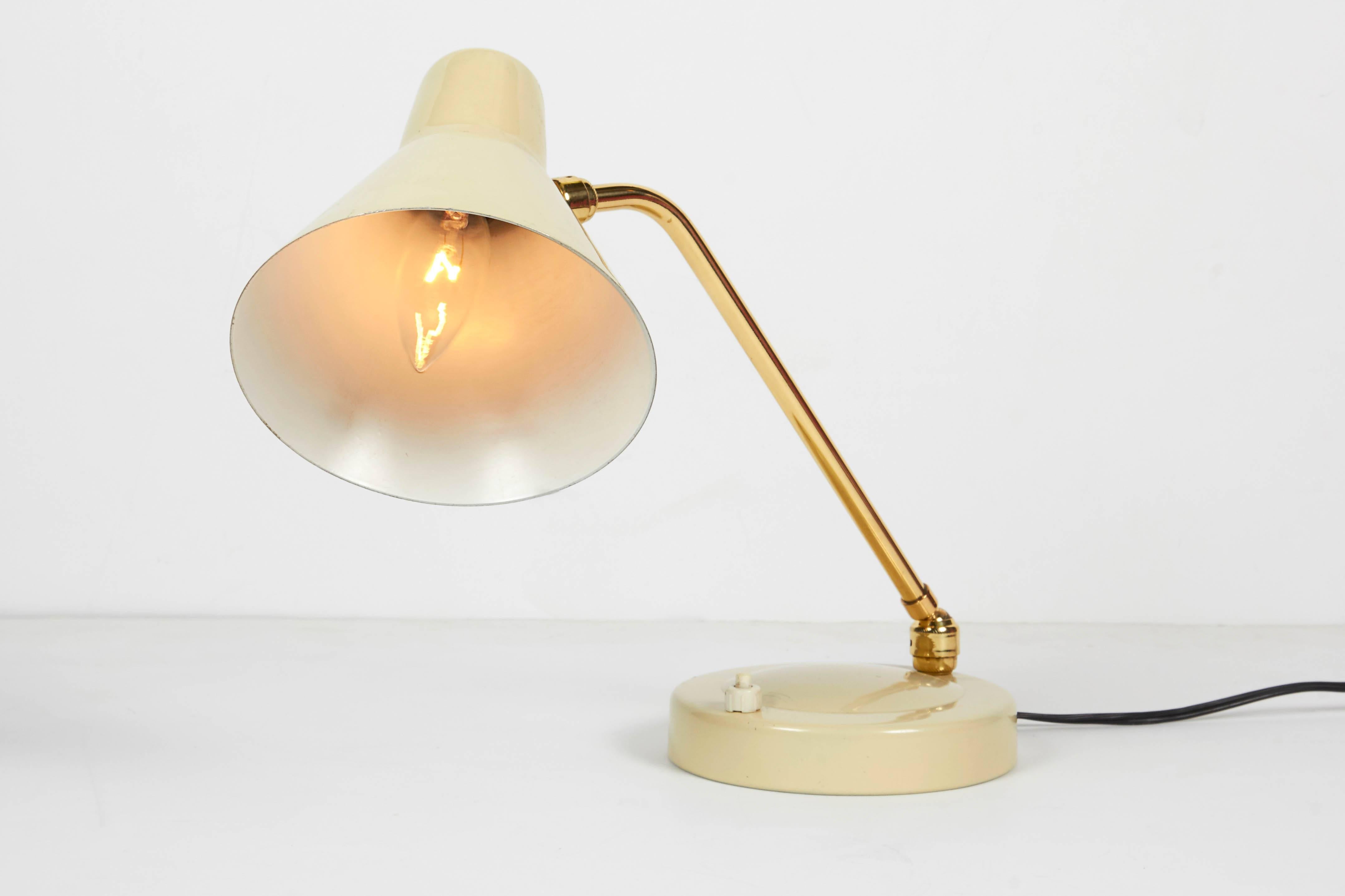 An Italian 1950s desk table lamp. Shade and base in an ivory enamel. Articulated brass support rod is adjustable along with the shade angle. Takes a candelabra bulb.