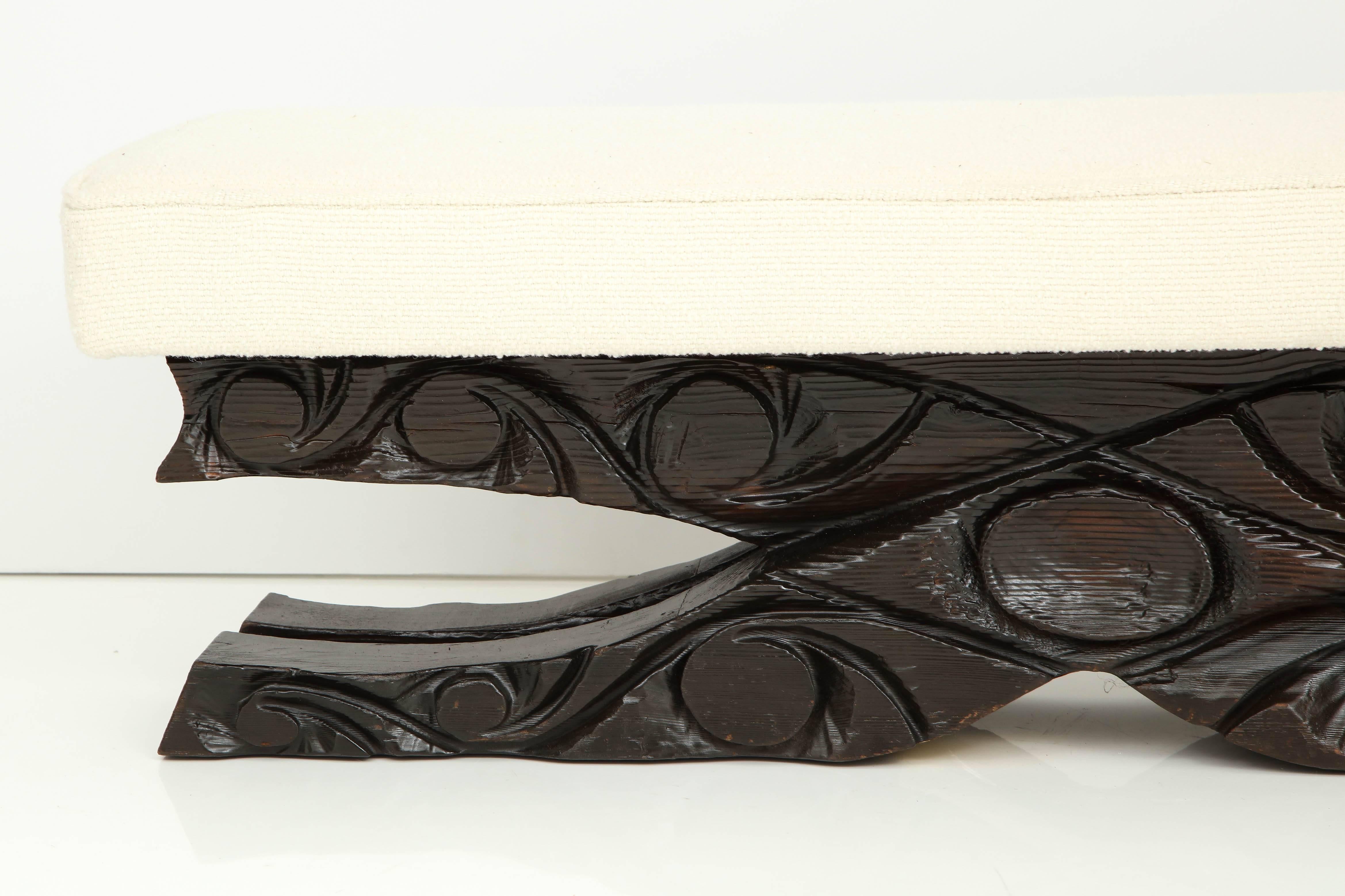 A carved pine bench with a blackened finish, upholstered in a Roger and Goffigon fabric.