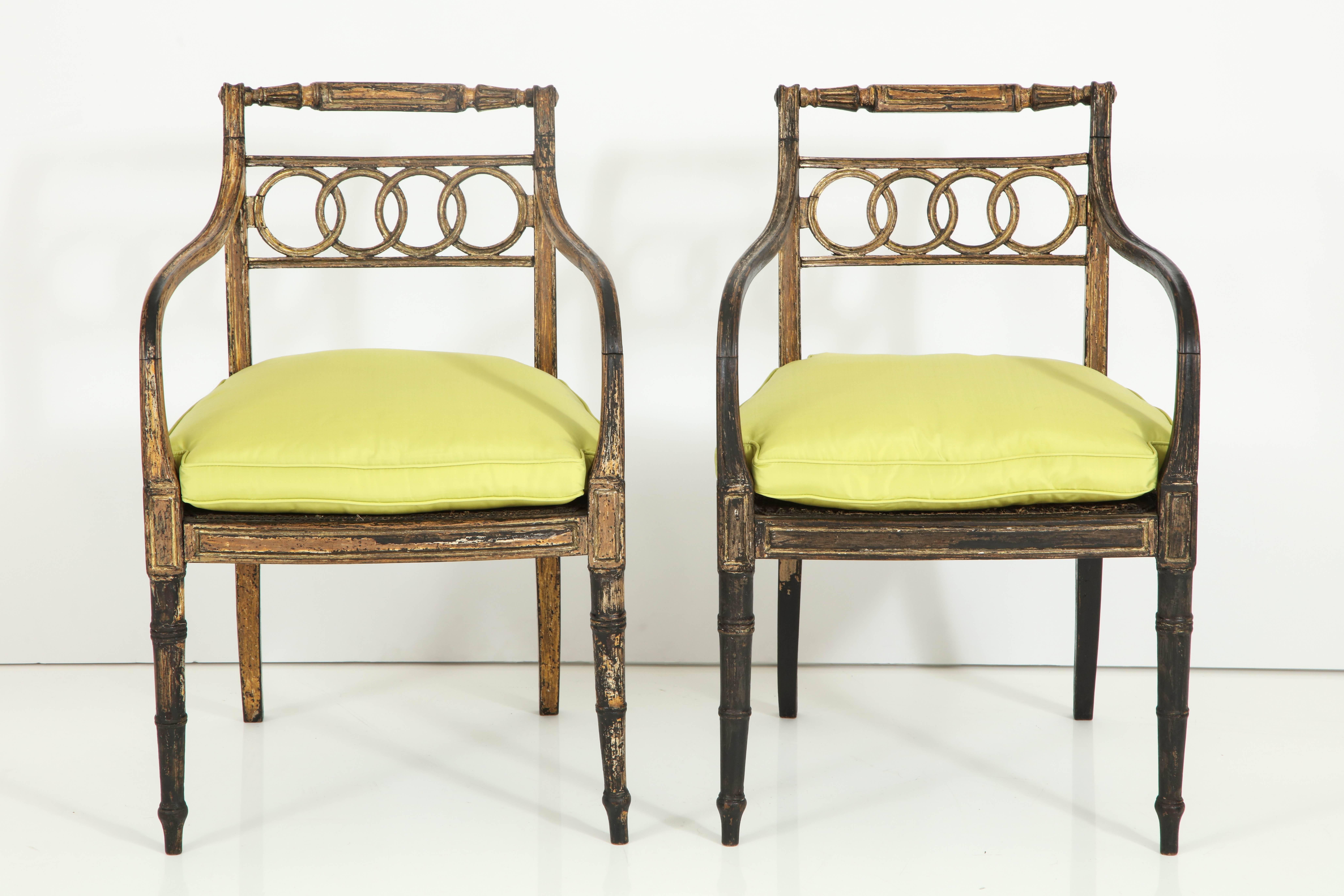 The detail and finish of these two chairs make them exceptional. Painted black with gold leaf accents, the chairs are replete with lovely neoclassical details, including the connecting rings on the back rest and the delicate turning on arms and