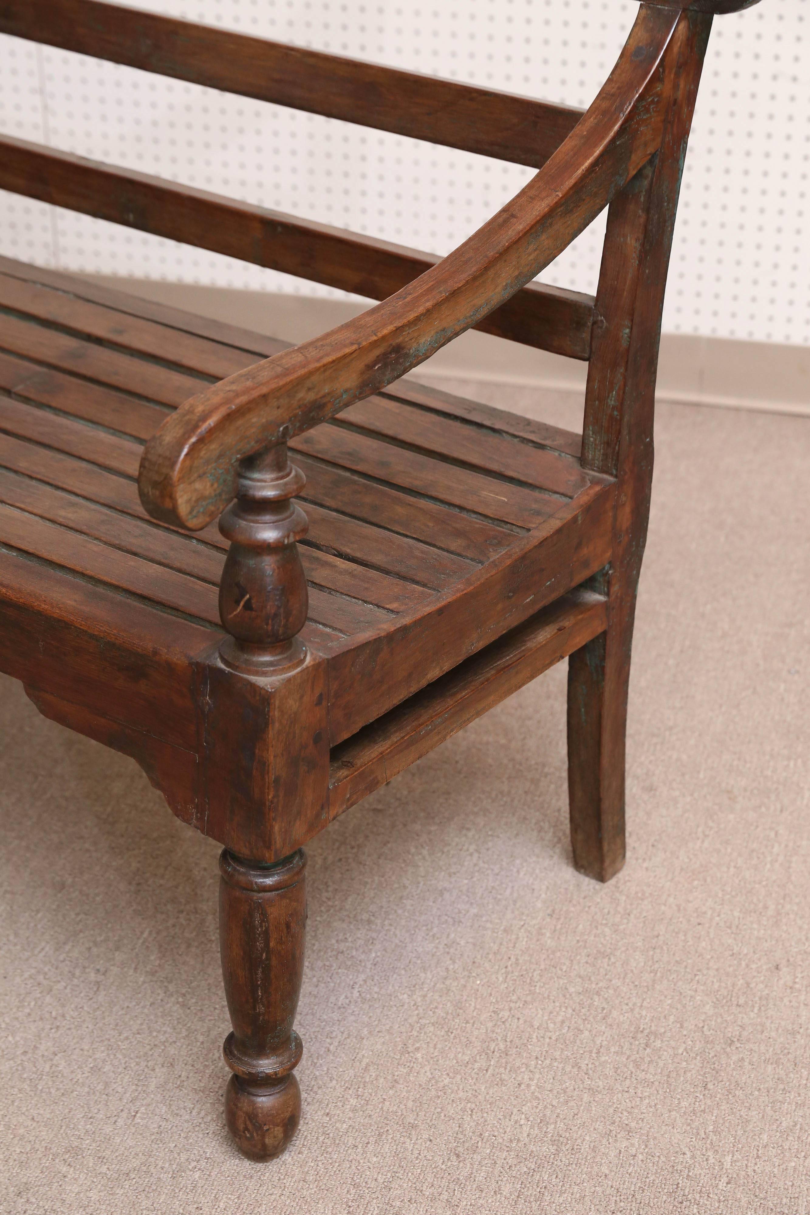 This is a 19th century, solid teak wood bench with five legs. It has armrest and a back support. It is contoured for comfort. Benches like this one were used in the corridors of colonial homes where they were partially exposed to the elements. The