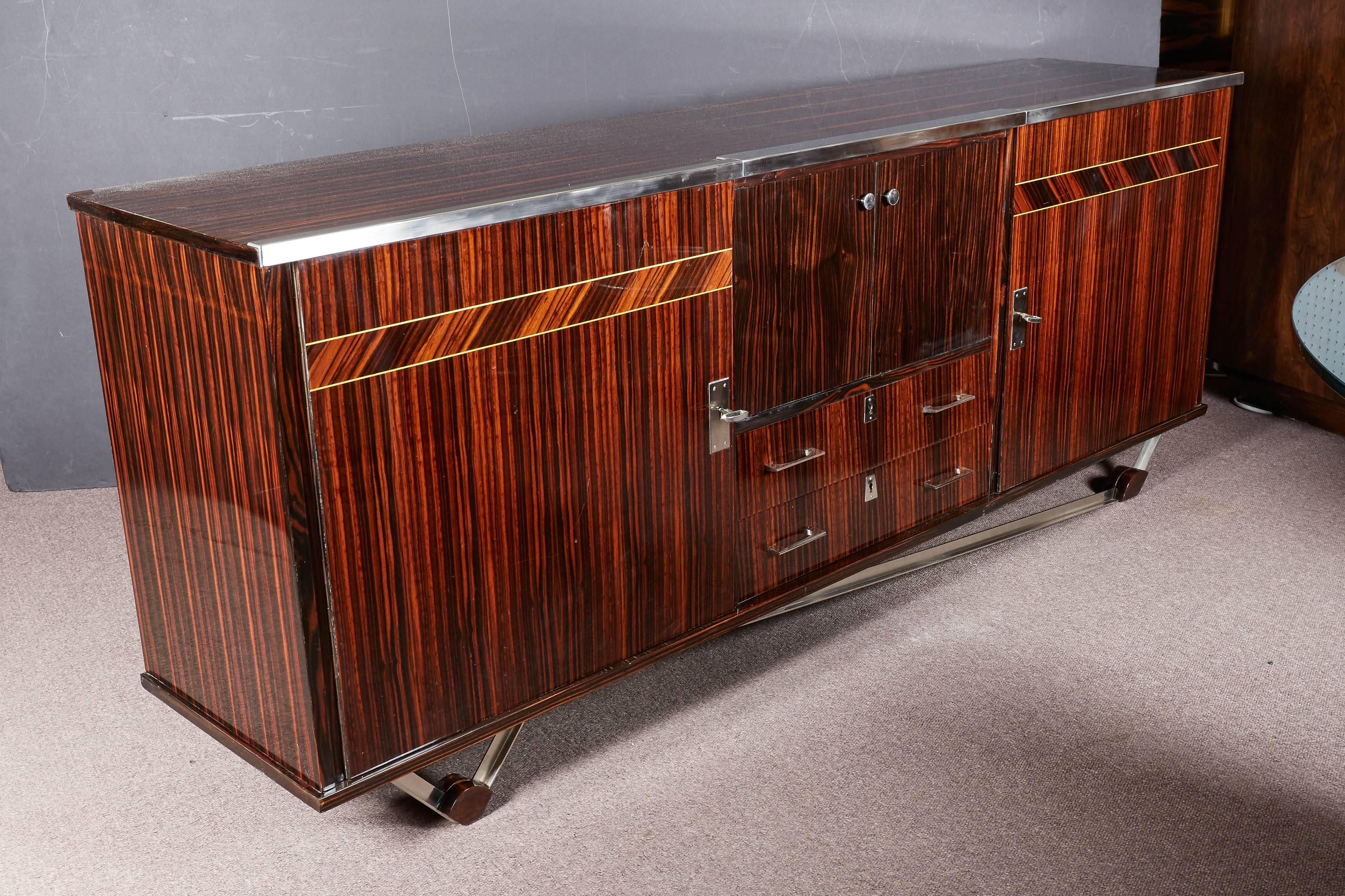 Fabulous French Art Deco high gloss lacquer exotic Macassar ebony buffet with geometric inlaid parquetry detail on doors and nickeled bronze top border, hardware and matching asymmetrical angular base.
This sleek, stream line sideboard or cabinet