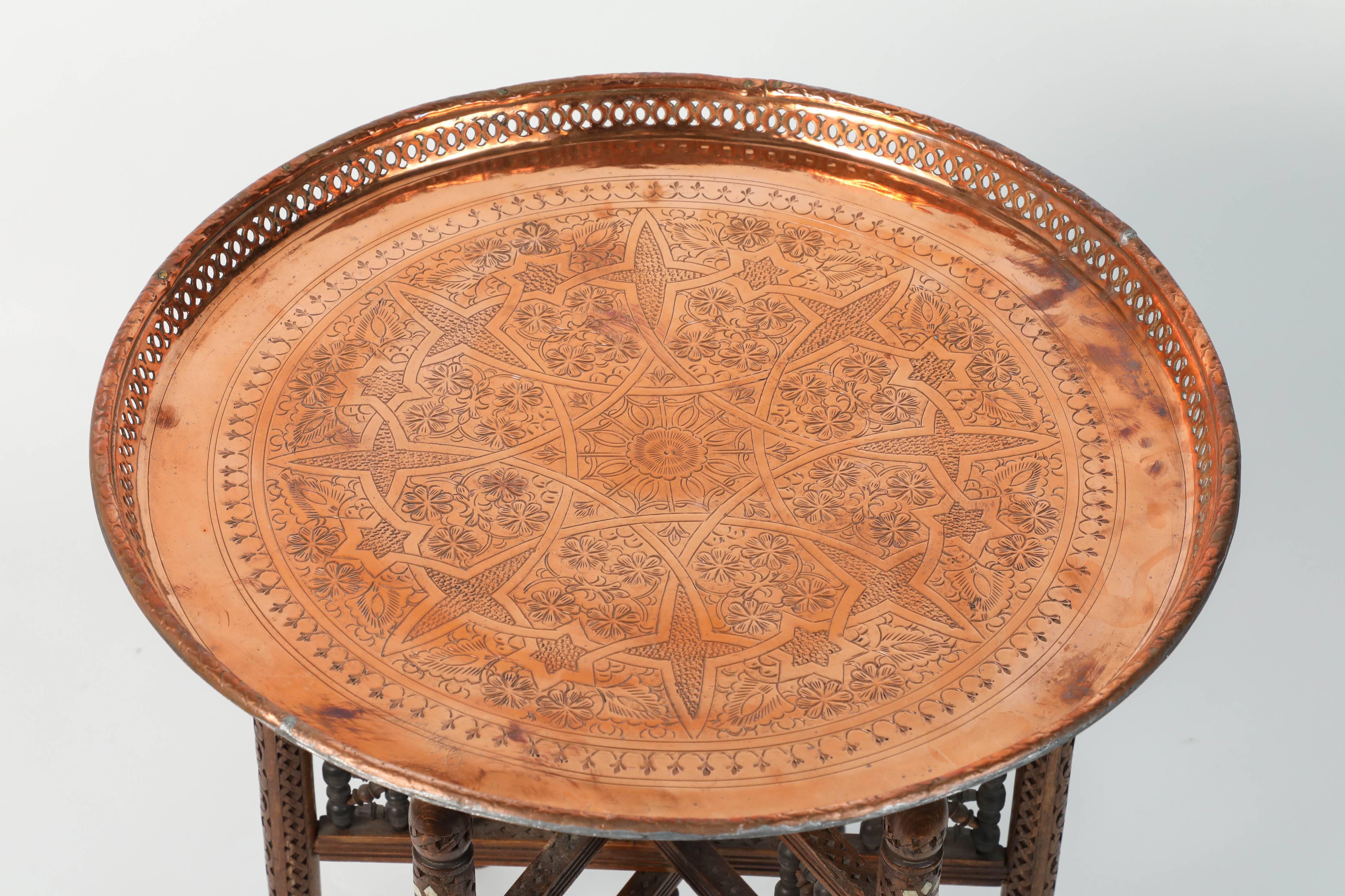 Table à plateau marocaine en cuivre ancien avec base pliante en bois sculpté à la main. 
Le plateau en cuivre martelé est décoré de motifs géométriques islamiques mauresques. 
Le plateau est amovible et se compose d'un plateau rond en cuivre