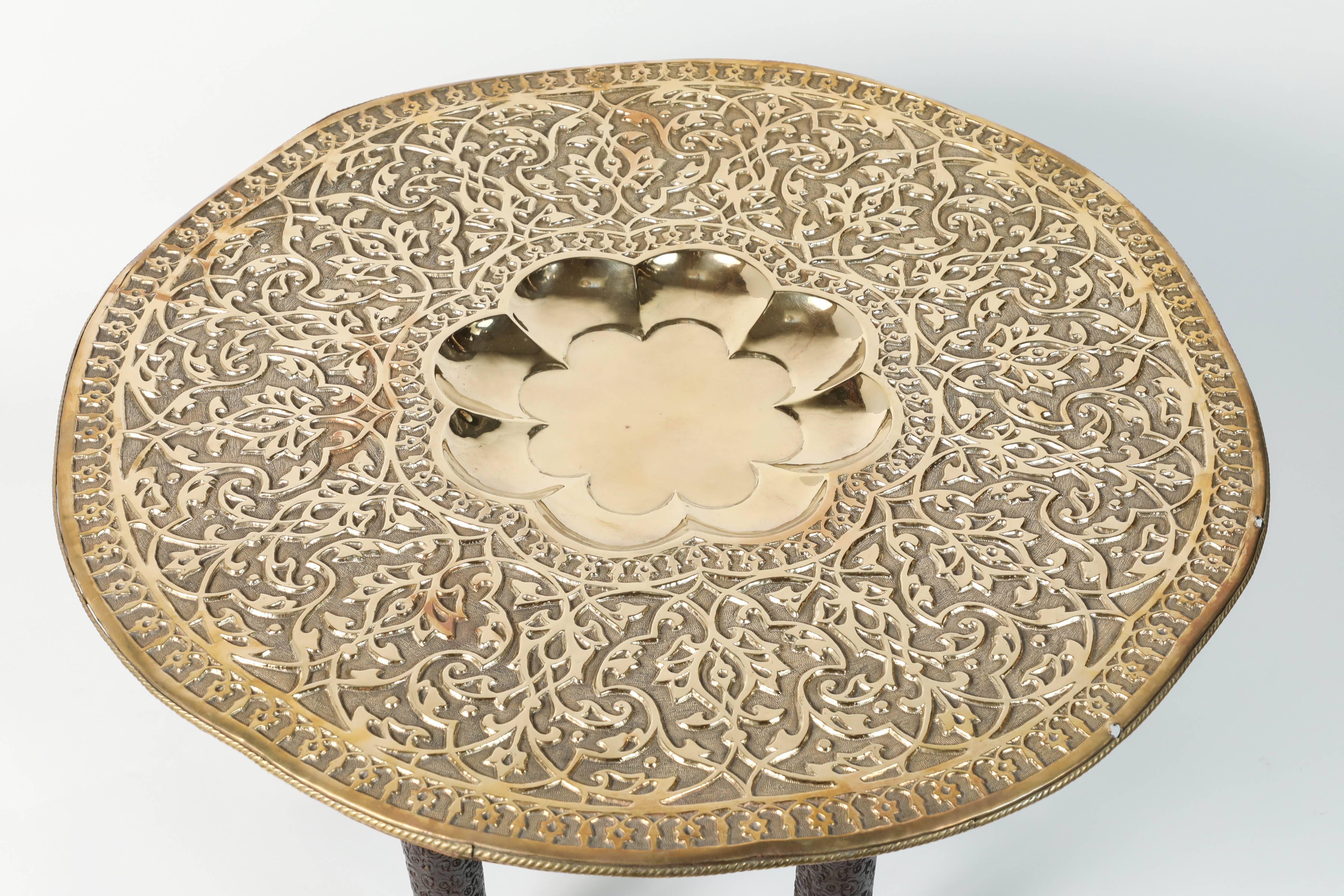 Mughal Empire antique brass tray table with carved wooden folding stand.
The Mughal style brass top is decorated with fine foliage and geometric Islamic Moorish designs.
The brass tray is decorated in repoussé floral and foliate motif.
The top is