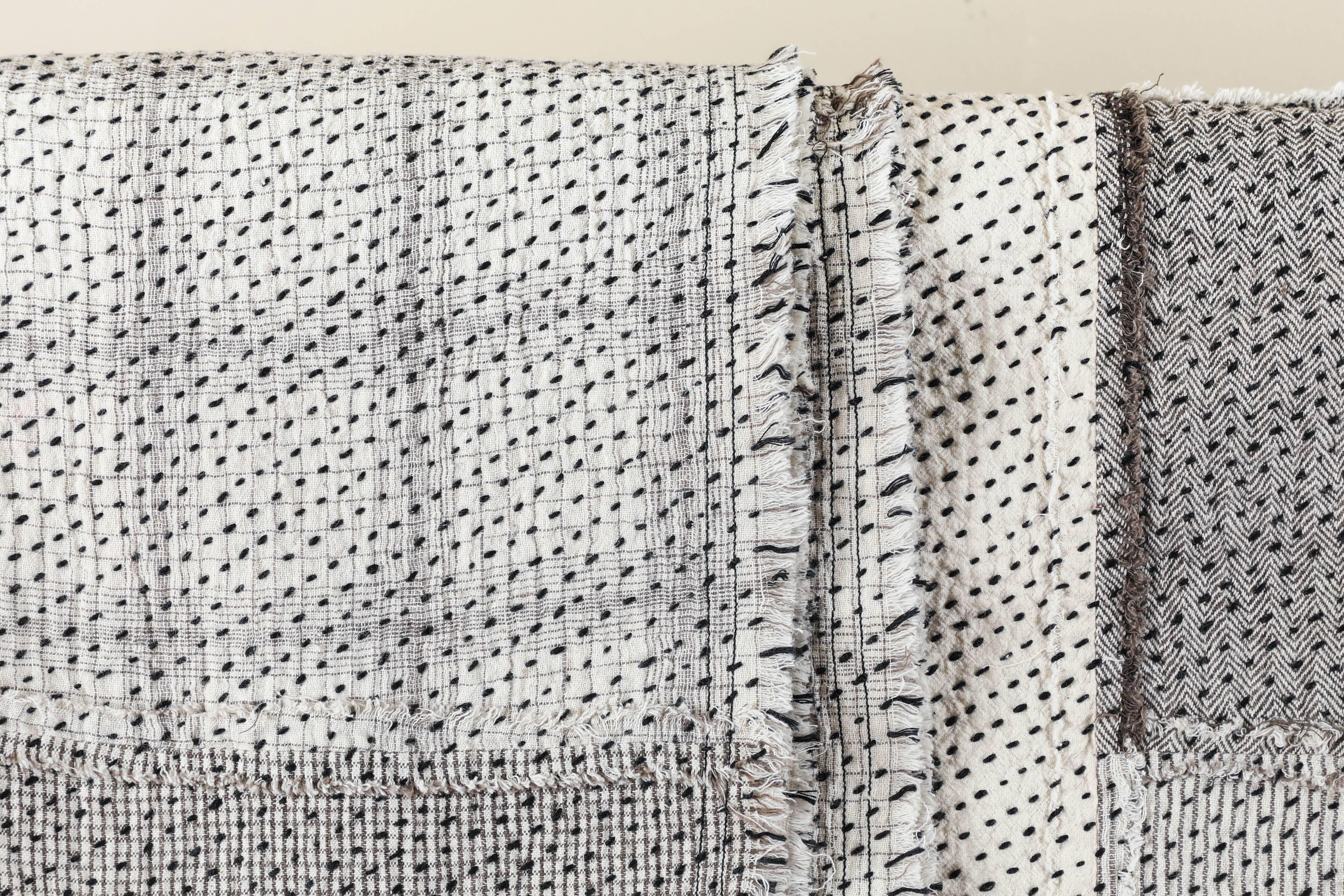 Contemporary handwoven and quilted Stitch by Stitch cotton quilt. Frayed edges. Patched pieces of cotton with ivory and black designs on one side and white khadi on the reverse. Black cotton quilting stitches. Handwoven, handmade in Gujarat, India.