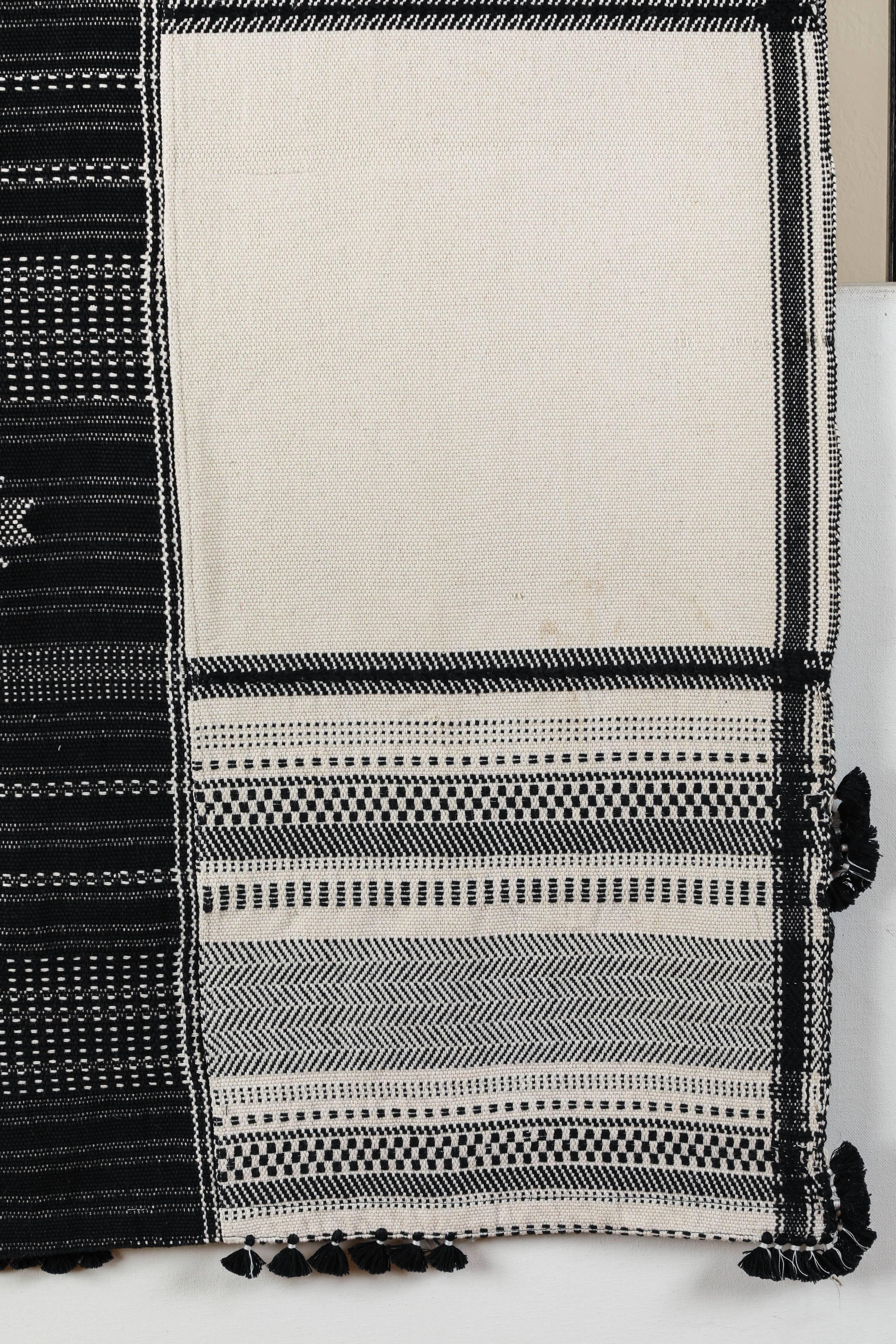 Kala naturally dyed organic cotton from Gujarat, India. Hand-loomed using traditional Indian textile techniques to produce extra weft woven stripes and plaids. This black and white bedcover has added hand-knotted tassels. Areas of hand embroidery