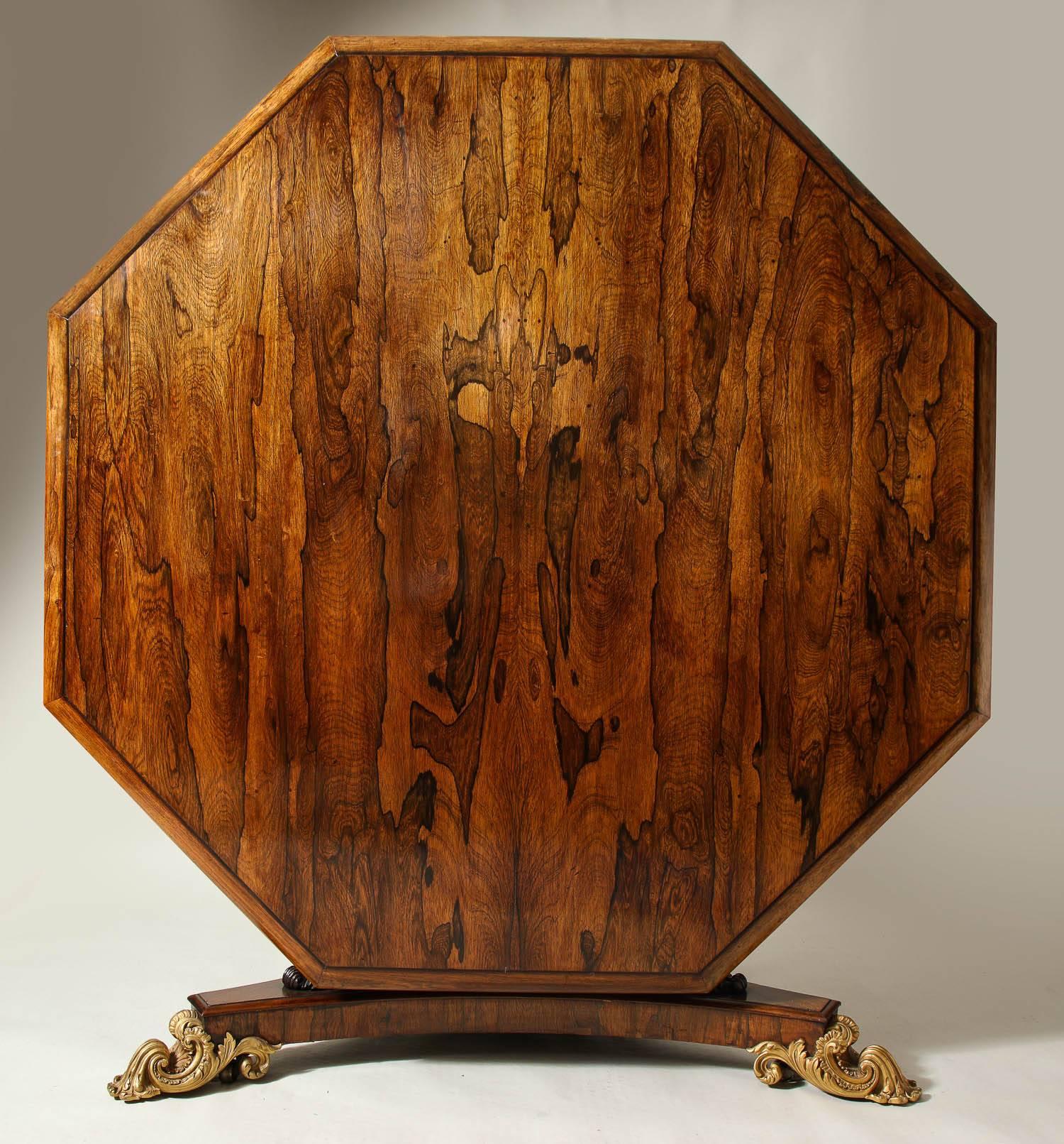 A very fine Regency rosewood centre table by Miles and Edwards, having an octagonal top with a molded edge over a parcel-gilt and carved rosewood pedestal ending in a tripartite base with gilt bronze acanthus leaf feet, the whole possessing vivid