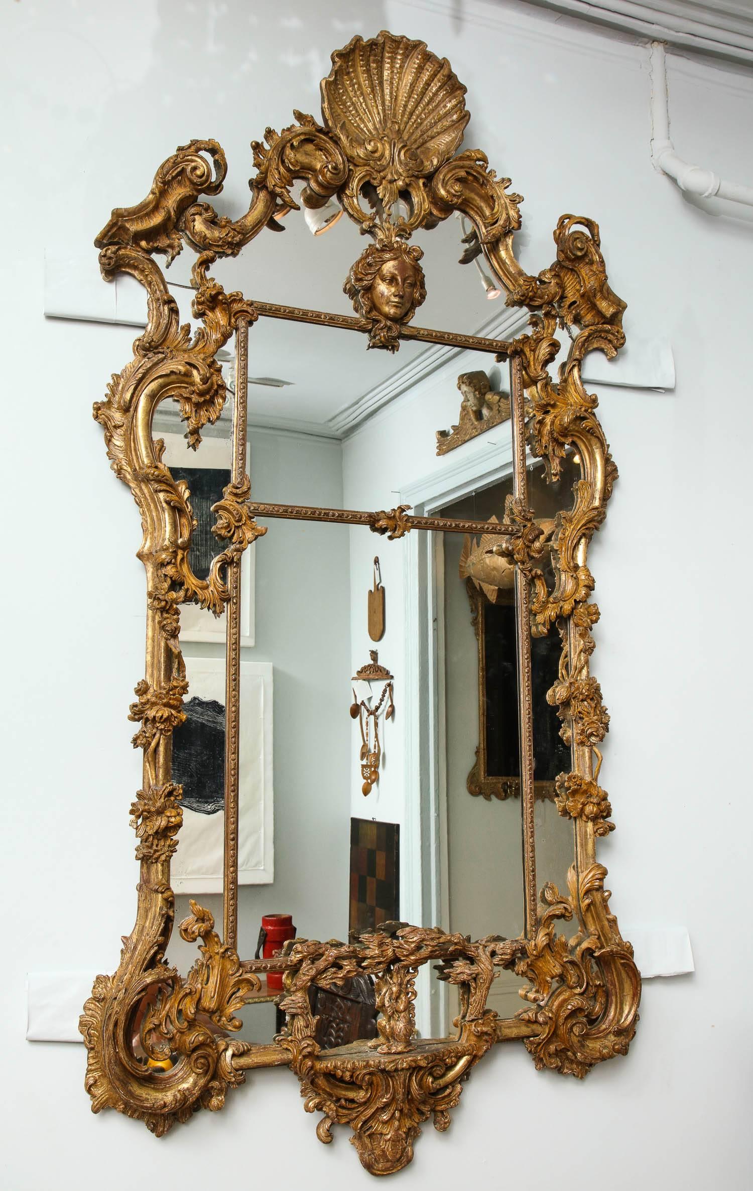 Fine George III style giltwood mirror in the manner of Thomas Johnson, the shell carved crest with foliate scrolled pediment, over a female mask, the sides with trailing flowering vines and scrolls, the lower border plate with central carving of a