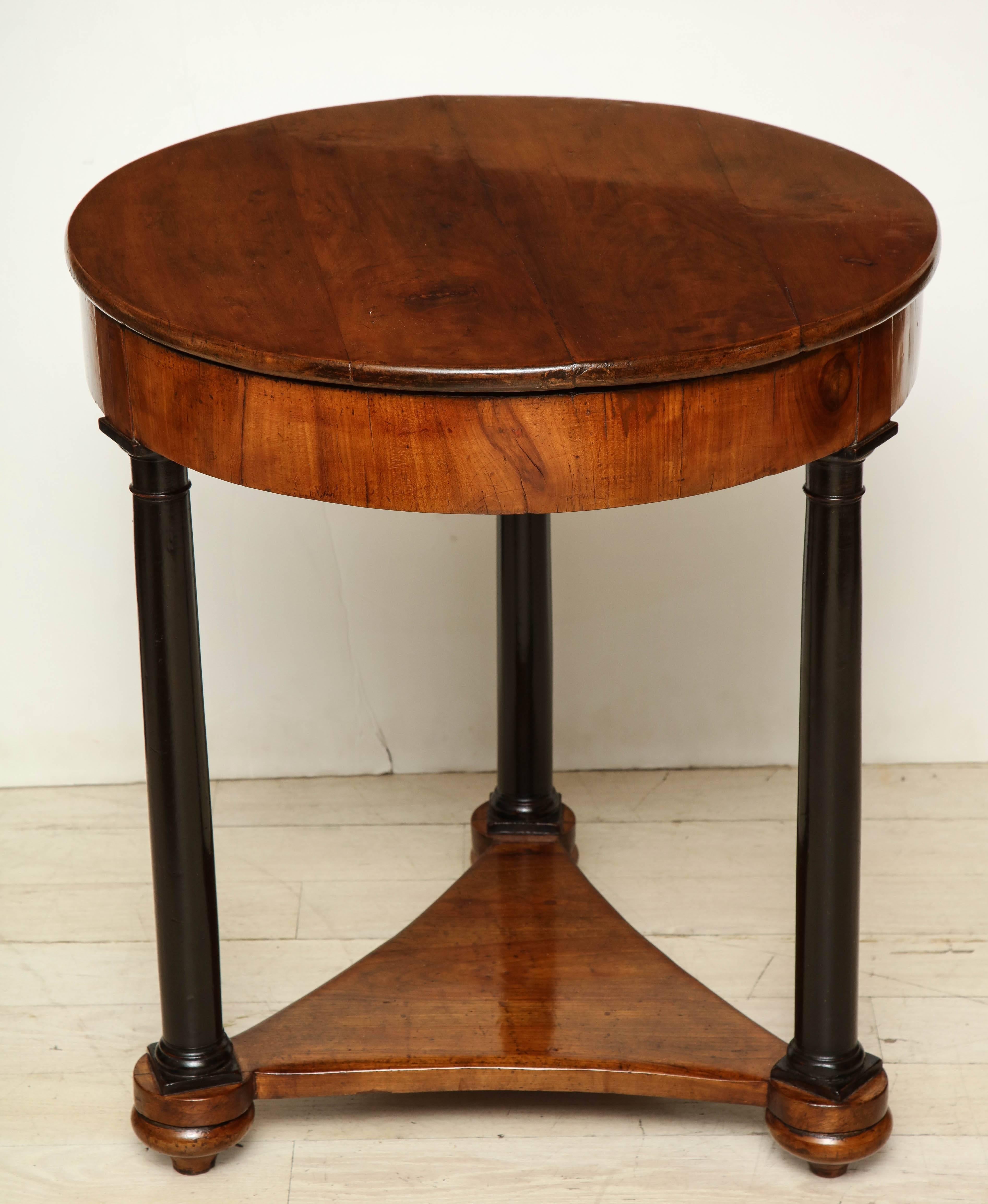 Early 19th-century circular cherry table with ebonized columnar supports and tripartite plinth base from the Veneto region. The hinged top opens to a 4 quadrant interior. Italy, circa 1810.