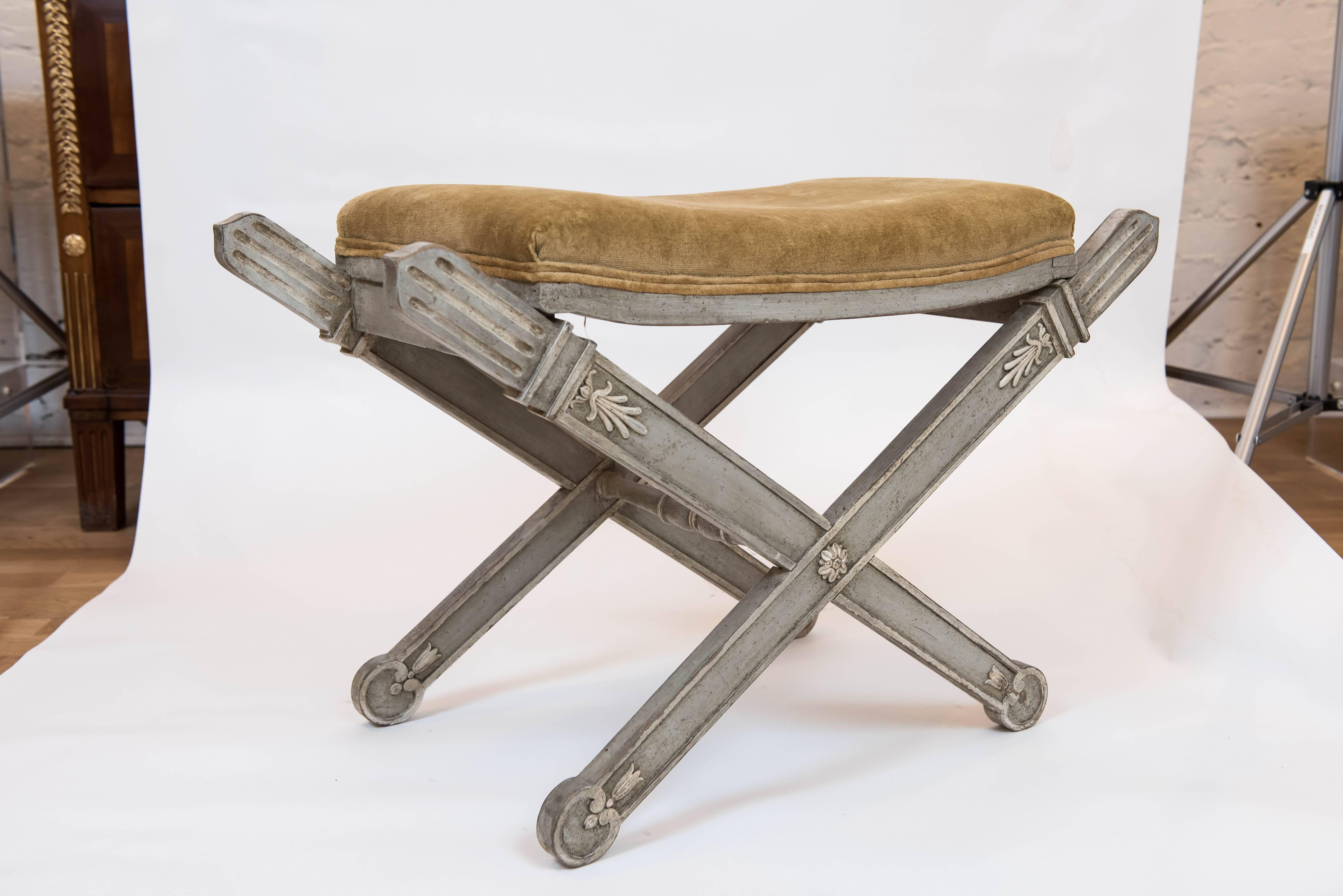 A highly decorative and beautiful grey-green neoclassical X-form bench with distressed white painted accents.
The upholstery is a 