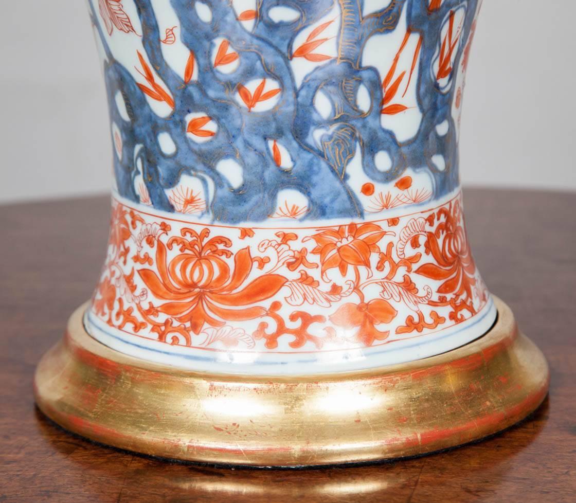 An highly decorative 18th century Chinese Imari porcelain vase decorated with sprays of flowers in blue and white, with orange details and gilt work dating from circa 1750. The vase has been fitted with a hand-carved and giltwood base. With antiqued