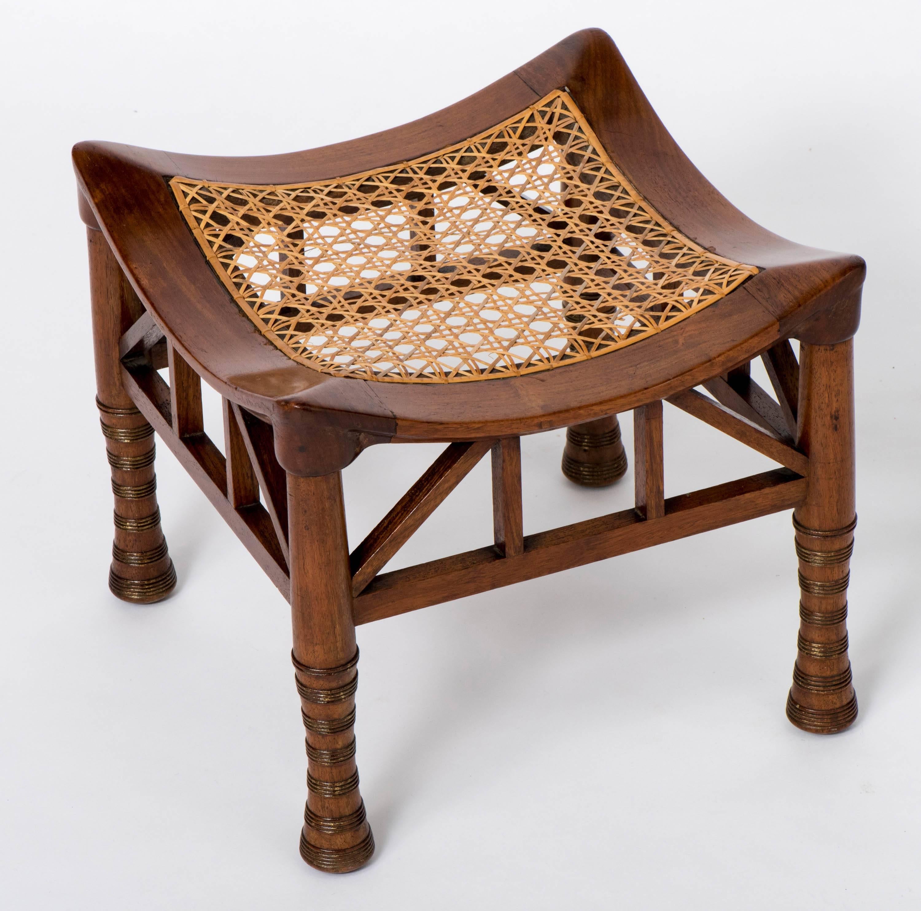 A walnut “Thebes” stool by Liberty and Co.
The dished seat with a caned panel on tapering ring turned legs linked by a spindle frieze.
England, circa 1900
Measure: 31 cm high x 35.5 cm wide x 34.5 cm deep.
 