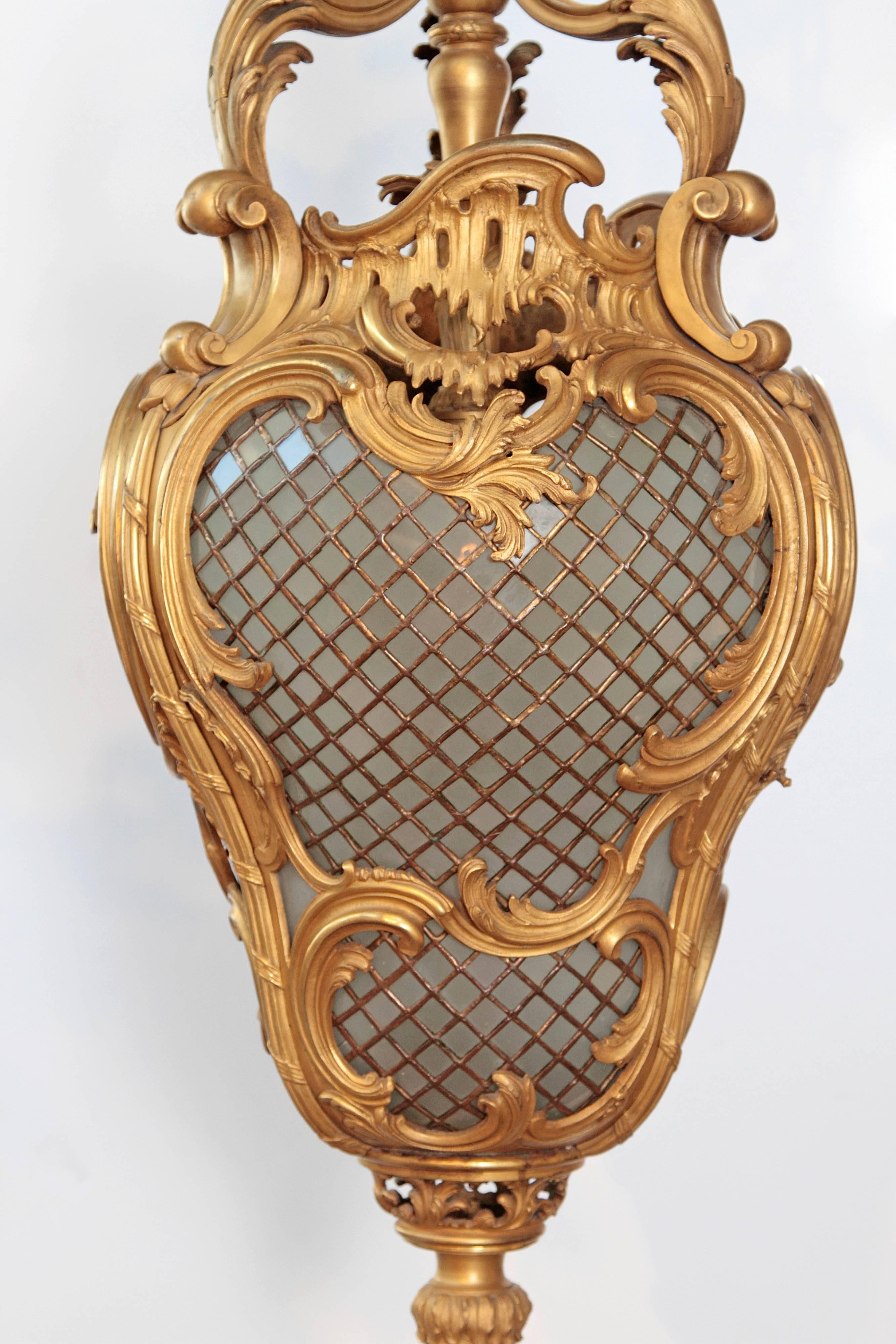 An elaborate 19th century gilt bronze hall lantern in the style of Louis XV. Curving ormolu at the top and sides of a rounded leaded glass body in a diamond pattern with more ormolu at the bottom, 19th century, France.