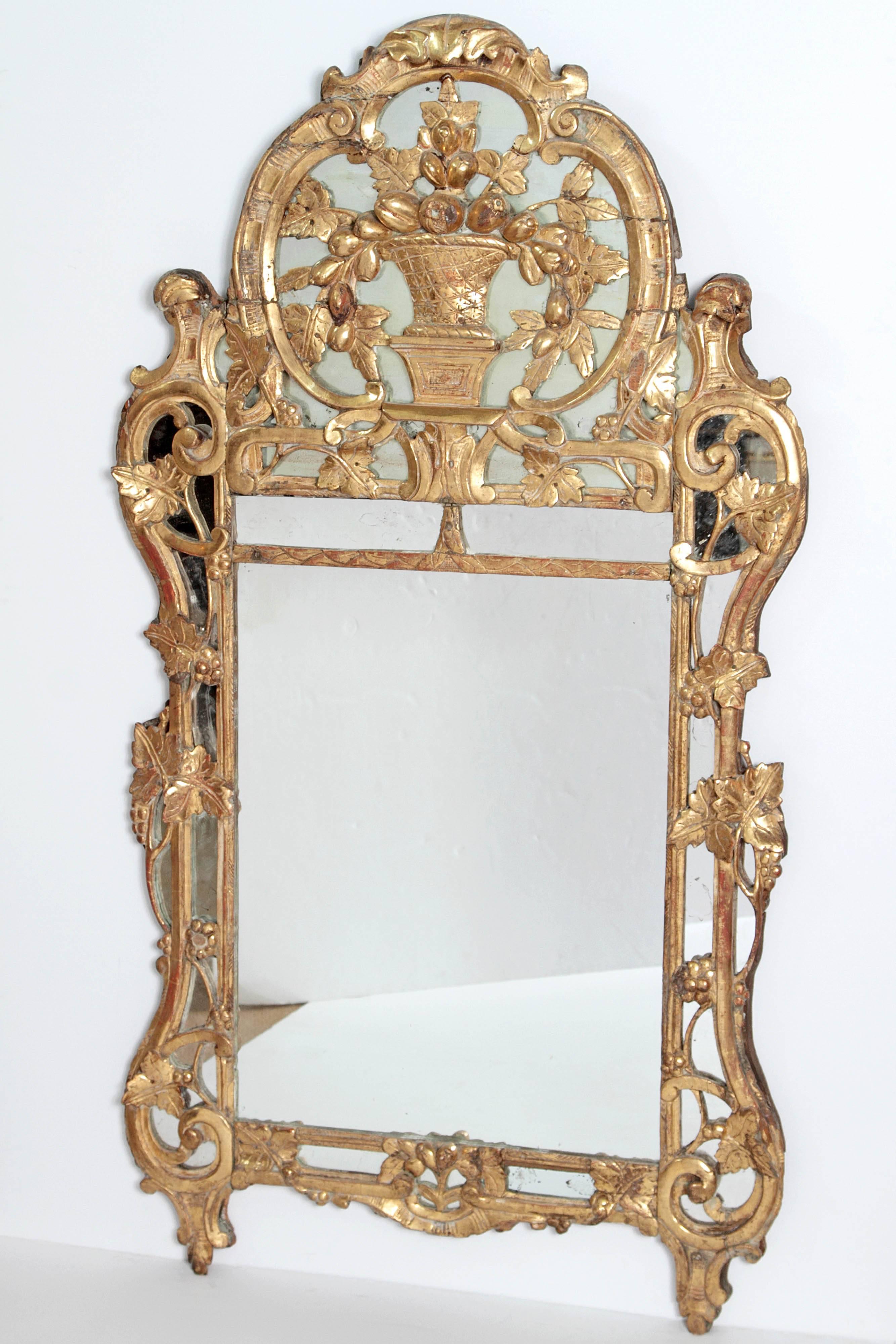 18th century Louis XV Provincial mirror in C-scroll carved wooden frames, with vine leaves, pierced and gilded, decorated with a stylized vase filled with foliage and seasonal fruit. The mirror is decorated with rocaille scrolls, vines, grapes and