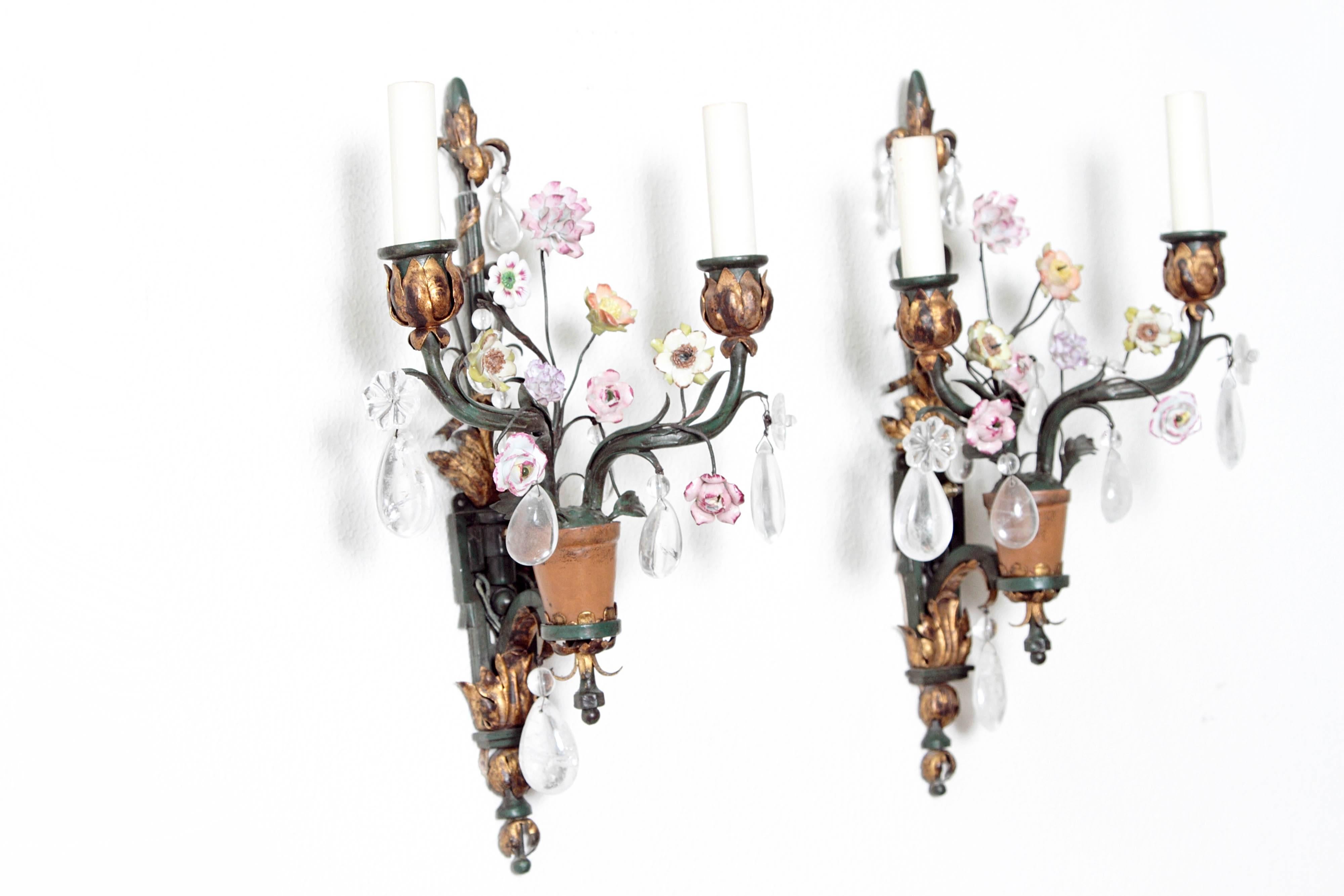 Whimsical pair of painted wrought iron two-arm wall lights depicting a pot of flowers, with porcelain flowers, rock crystal drops and gilded accents.
France, 1920s
Possible Bagues.