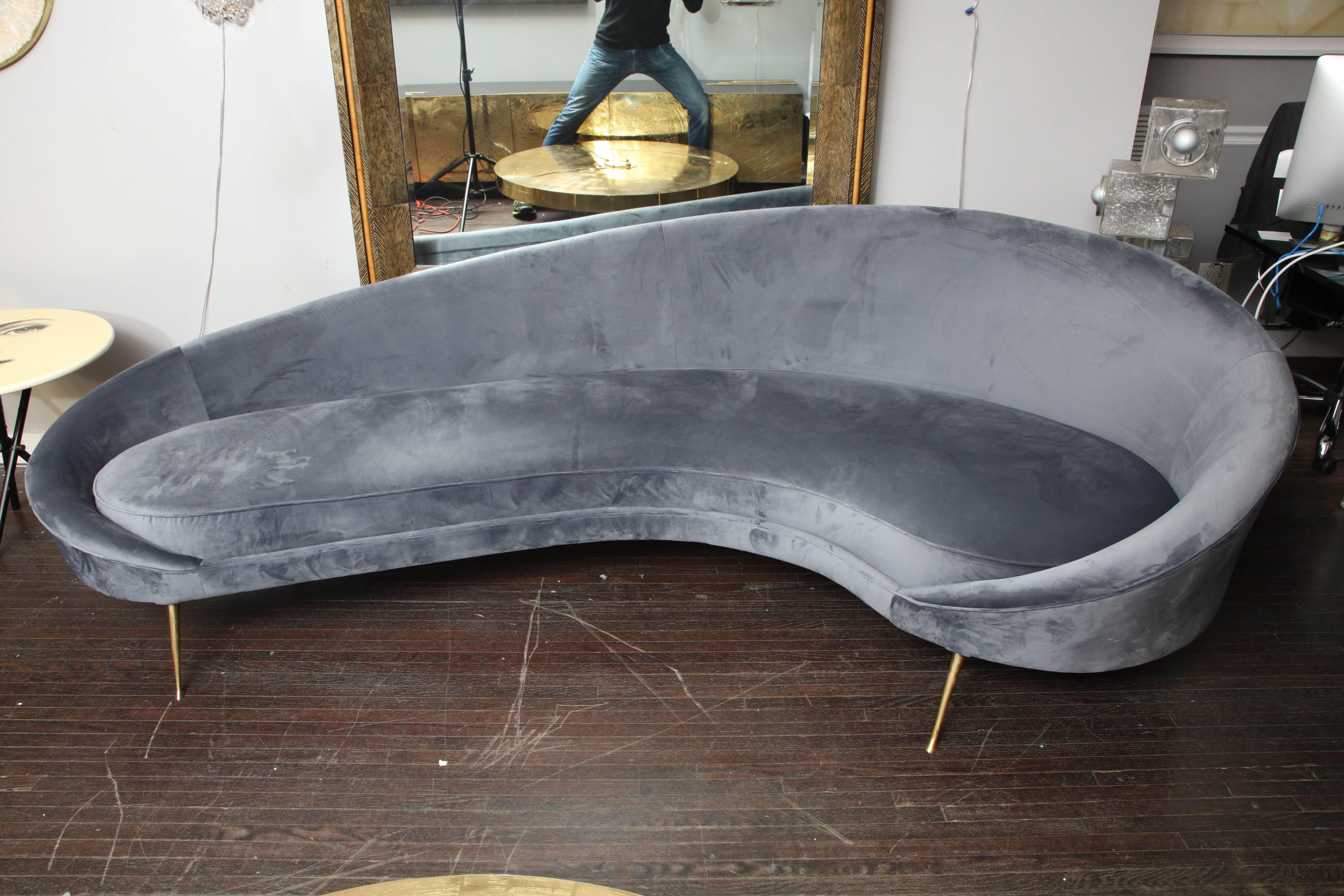 Elegant Mid-Century style Italian curved sofa in grey velvet. This is a floor sample that is available for immediate purchase as is. Minimum wear on fabric and scratches on legs. The seat depth varies from 20