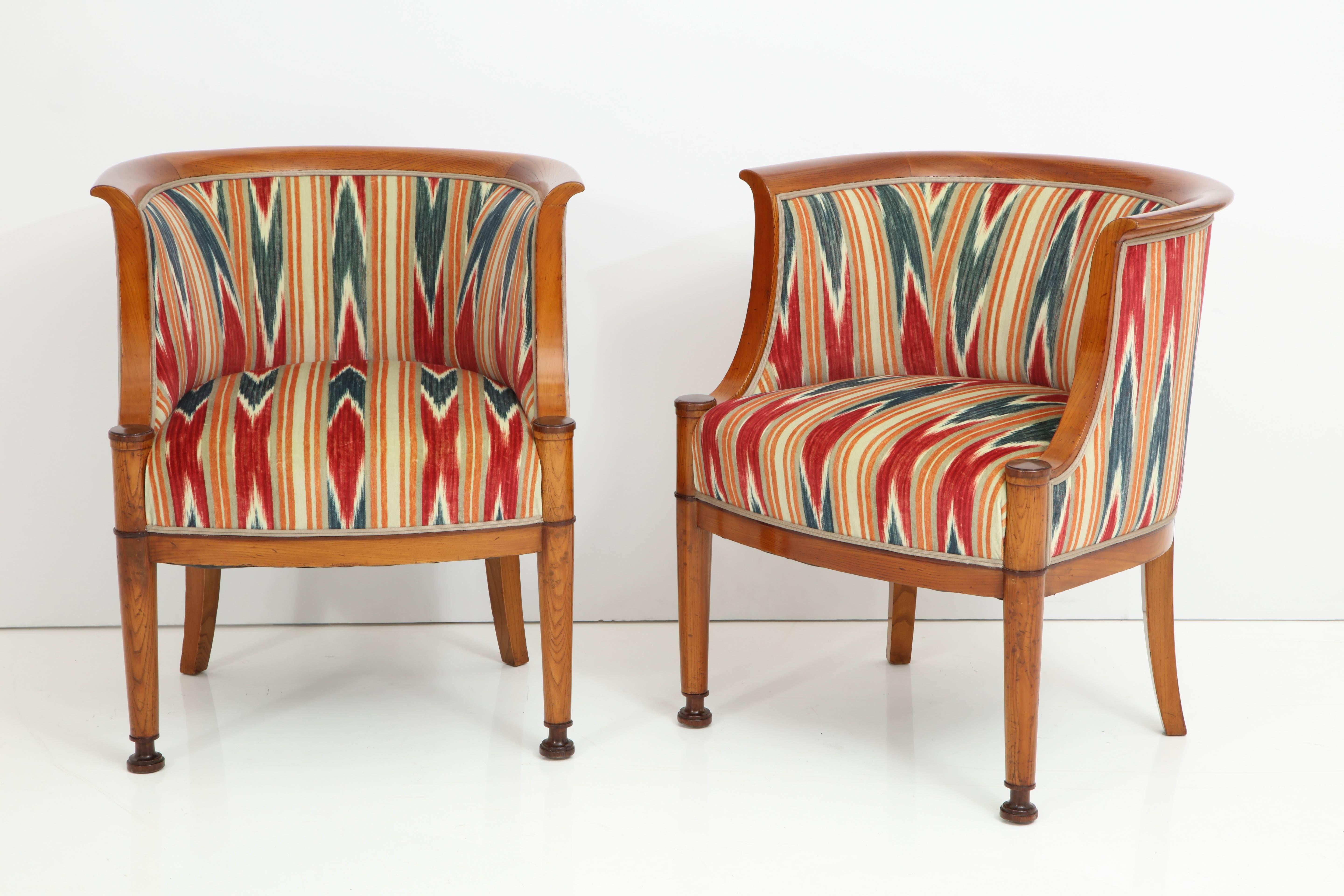 A pair of Danish polished elmwood and dark stained barrel back armchairs, circa 1910, each with a hoop backrest, scrolled supports raised on turned and tapered legs with dark stained banding and feet.