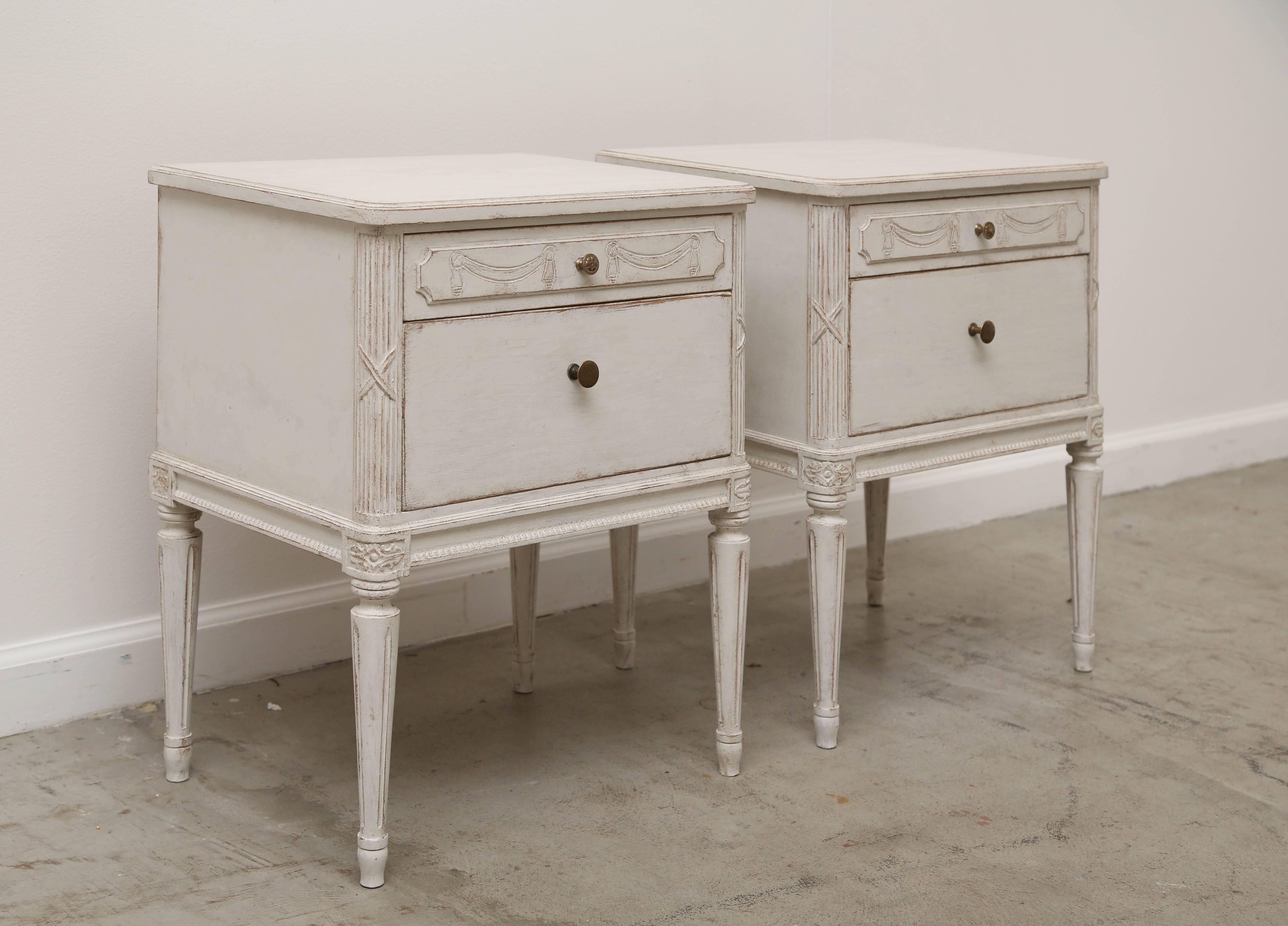 Pair of antique Swedish bedside chests painted distressed Swedish
White finish, two drawers, top drawer has carved swag and tassel
details, the corners are carved with ribbon and fluted .
Chest have fluted tapered legs, 
Early 20th century,