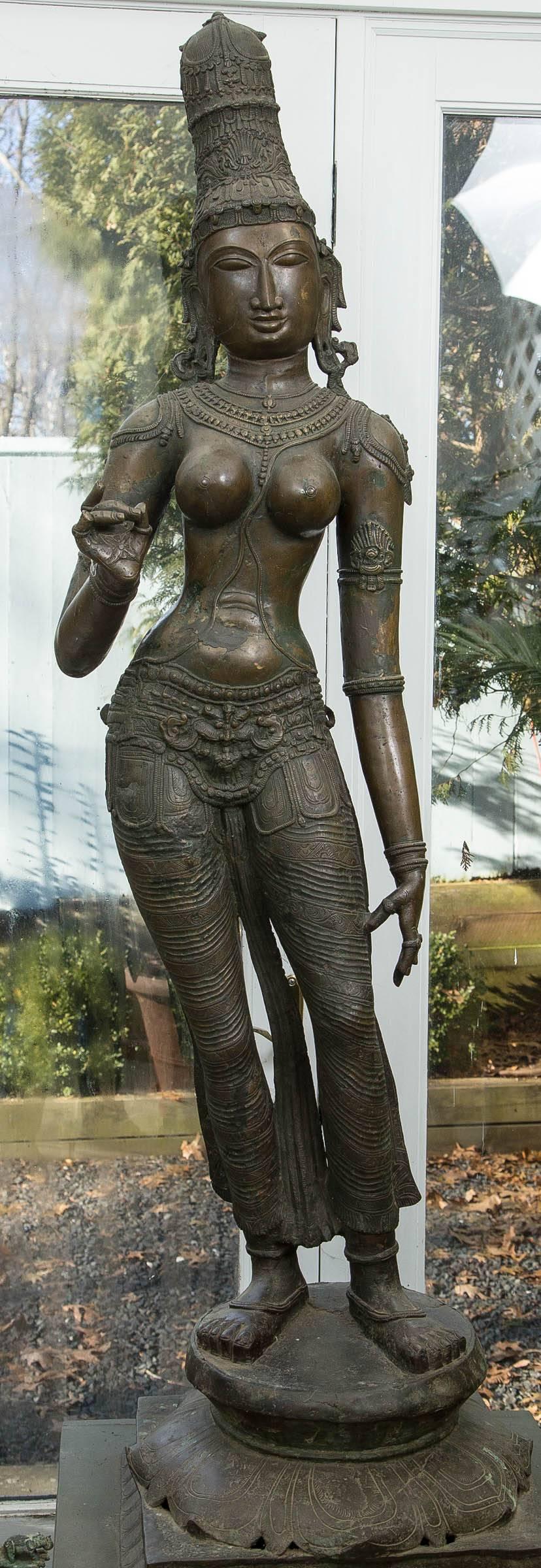 elegantly cast standing in a tribhangapose,  atop a  lotus base over a  waisted  plinth.  She is dressed  in a  long dhoti incised  with  foliate  patterns  tied  at the waist with a  pendant belt.  She is further adorned with beaded jewelry. An