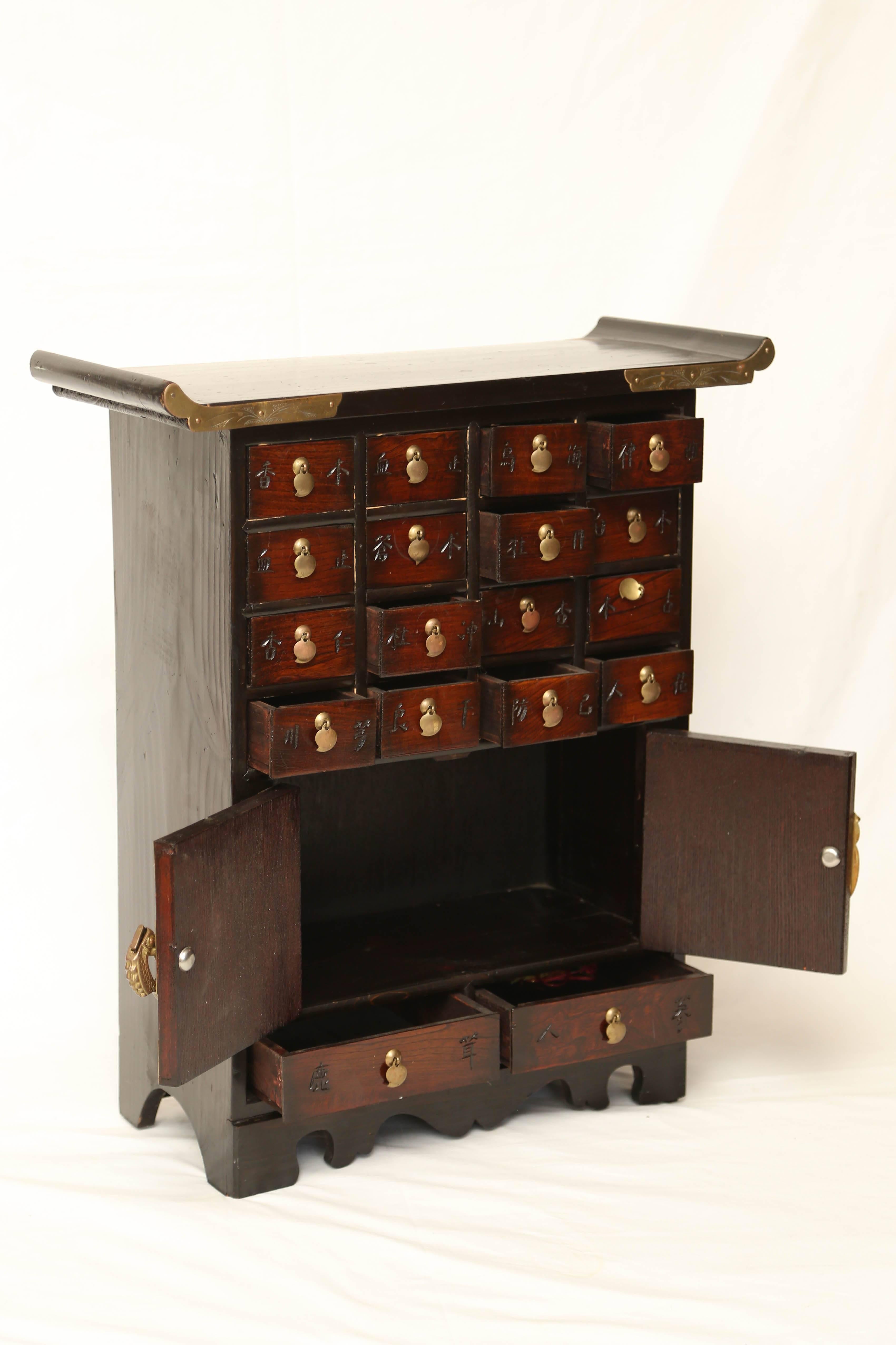 Small Asian multi drawer apoticary cabinet also perfect for jelewy too. Decorated with Asian characters, brass butterfly hinges, figural fish lock. Dimensions: H: 24.5 inches: W 21.25 inches, D 9 inches.