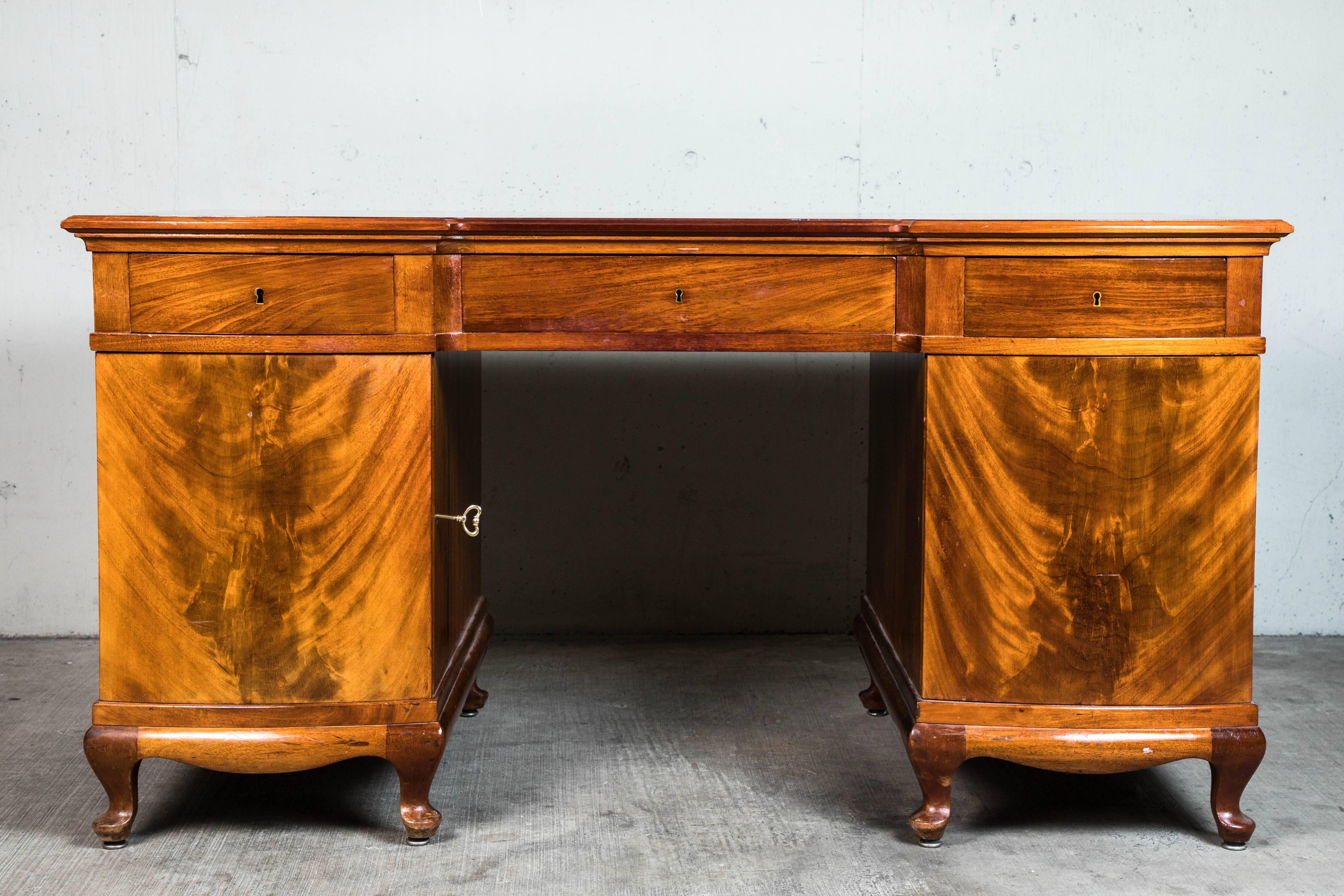 1940s mahogany desk with carved feet and eight drawers. Each side of drawers opens with a key.