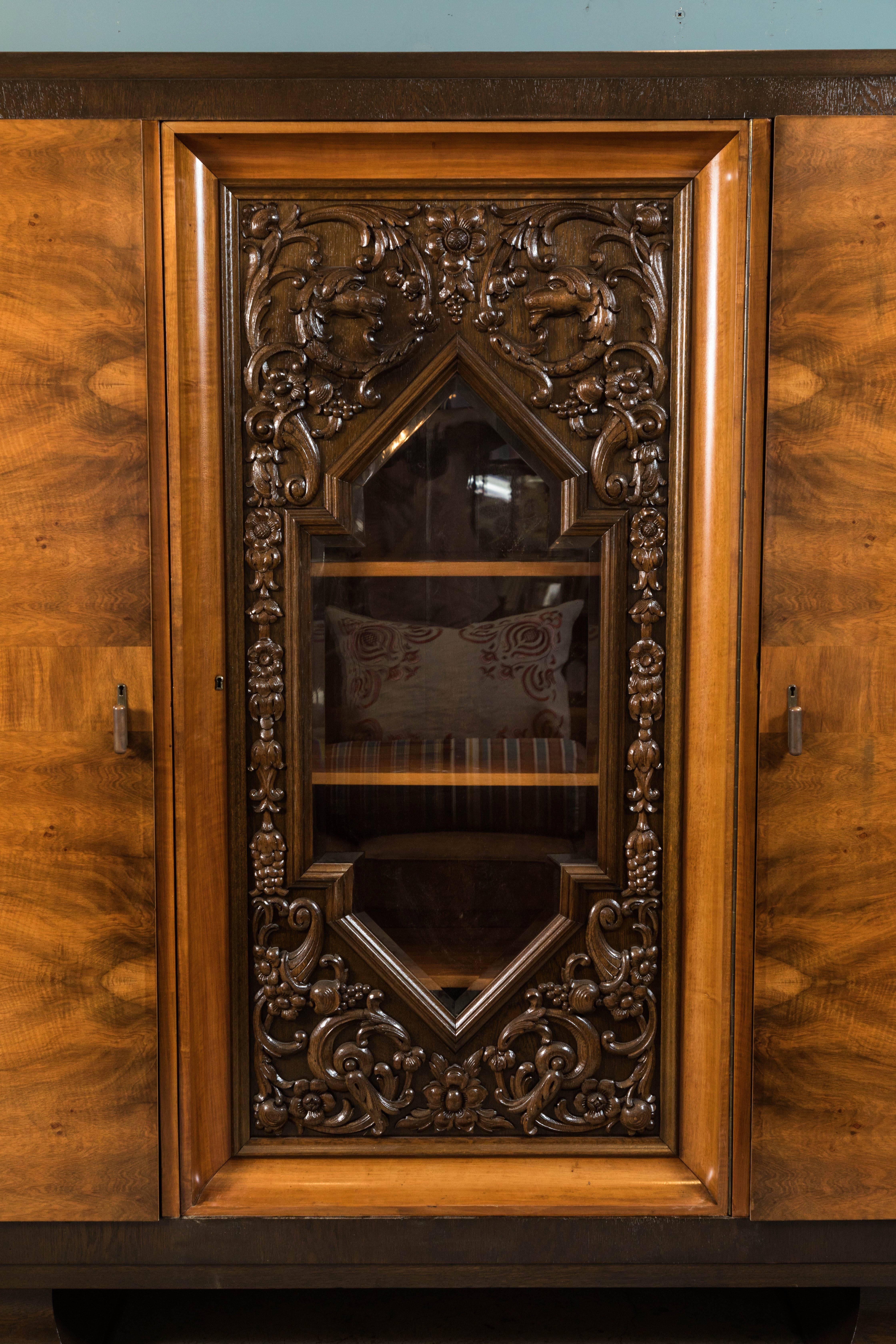 1930s-1940s walnut and oak three-door armoire. Centre door has a cut out centre with bevelled glass and ornate carved detail. All three sections have storage shelves inside. This piece has been completely stripped and newly refinished. Made in