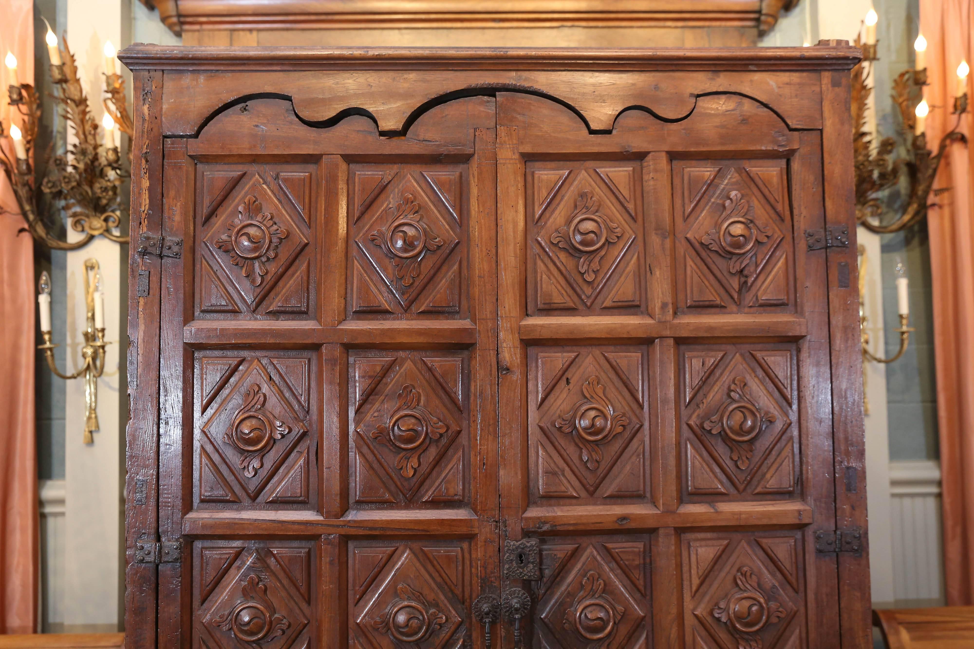 Early 17th century Colonial English oak armoire sits upon a carved stand.
The doors feature a 16 diamond shaped beveled panels surrounded by triangles in each corner. Rosettes surrounded by four carved leaves.
Top of doors are scalloped in a