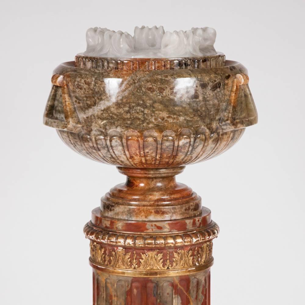 A carved green veined alabaster bowl of classical form, the covering white alabaster lid in the form of stylised flames, standing on a gilt and simulated marble fluted column.

Inside the bowl is a fitting for a light which enabling the bowl and